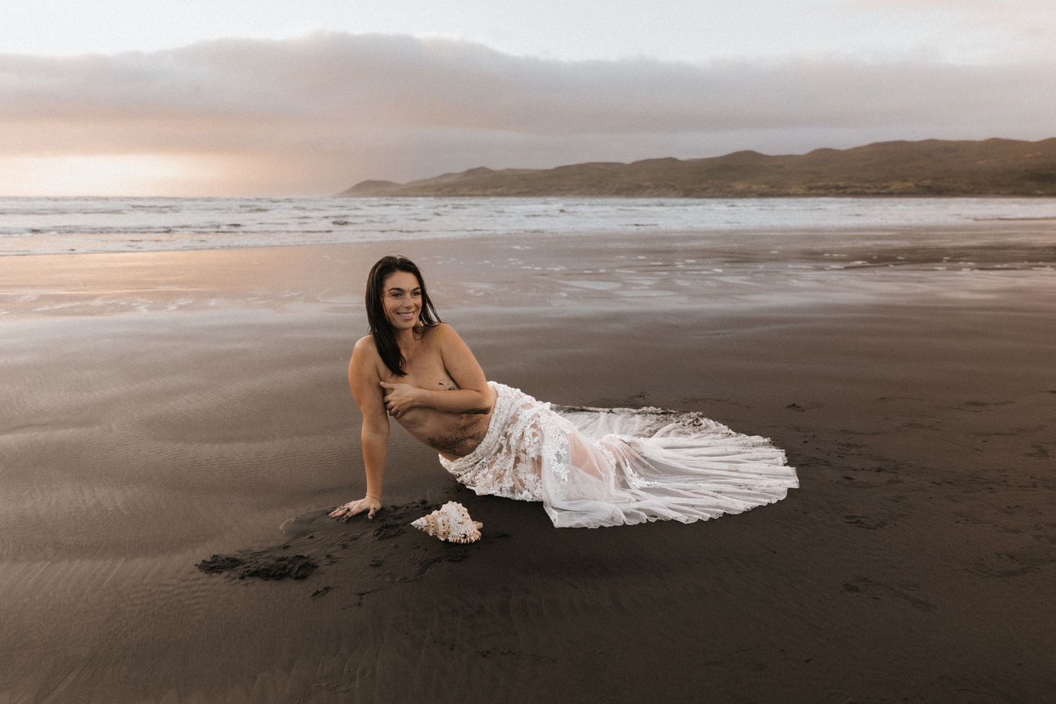 Artistic beach scene with flowing white dress against dramatic sunset sky.