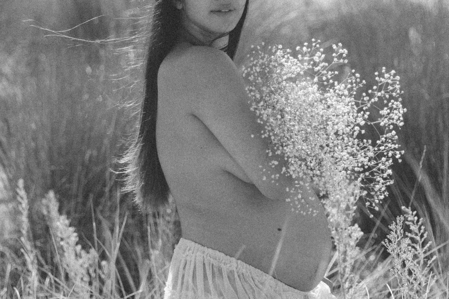Black and white maternity portrait with delicate flowers against rustic backdrop.