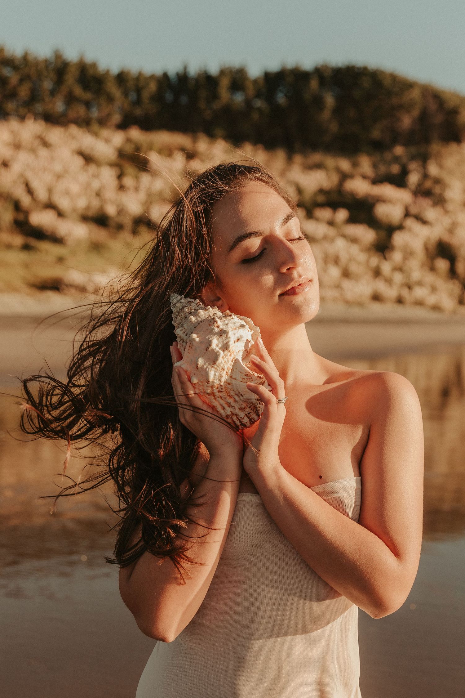 A dreamy beach photoshoot with seashells and warm sunset lighting creating an ethereal mood.