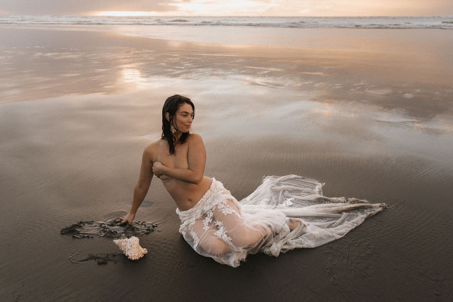 Moody coastal scene with white gown spread across dark volcanic sand at dusk.