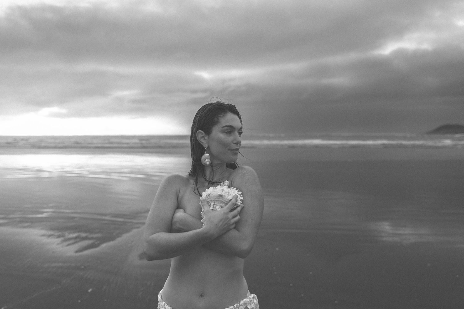 Black and white beach photography with dramatic cloudy sky and ocean waves.