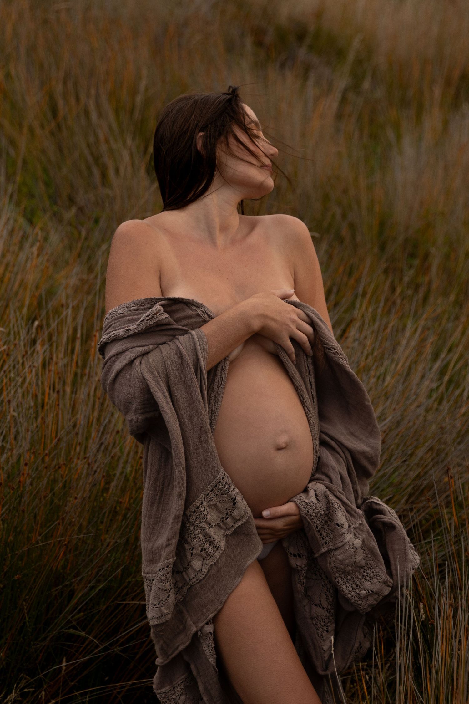 Intimate maternity portrait with brown lace wrap in natural grass setting.