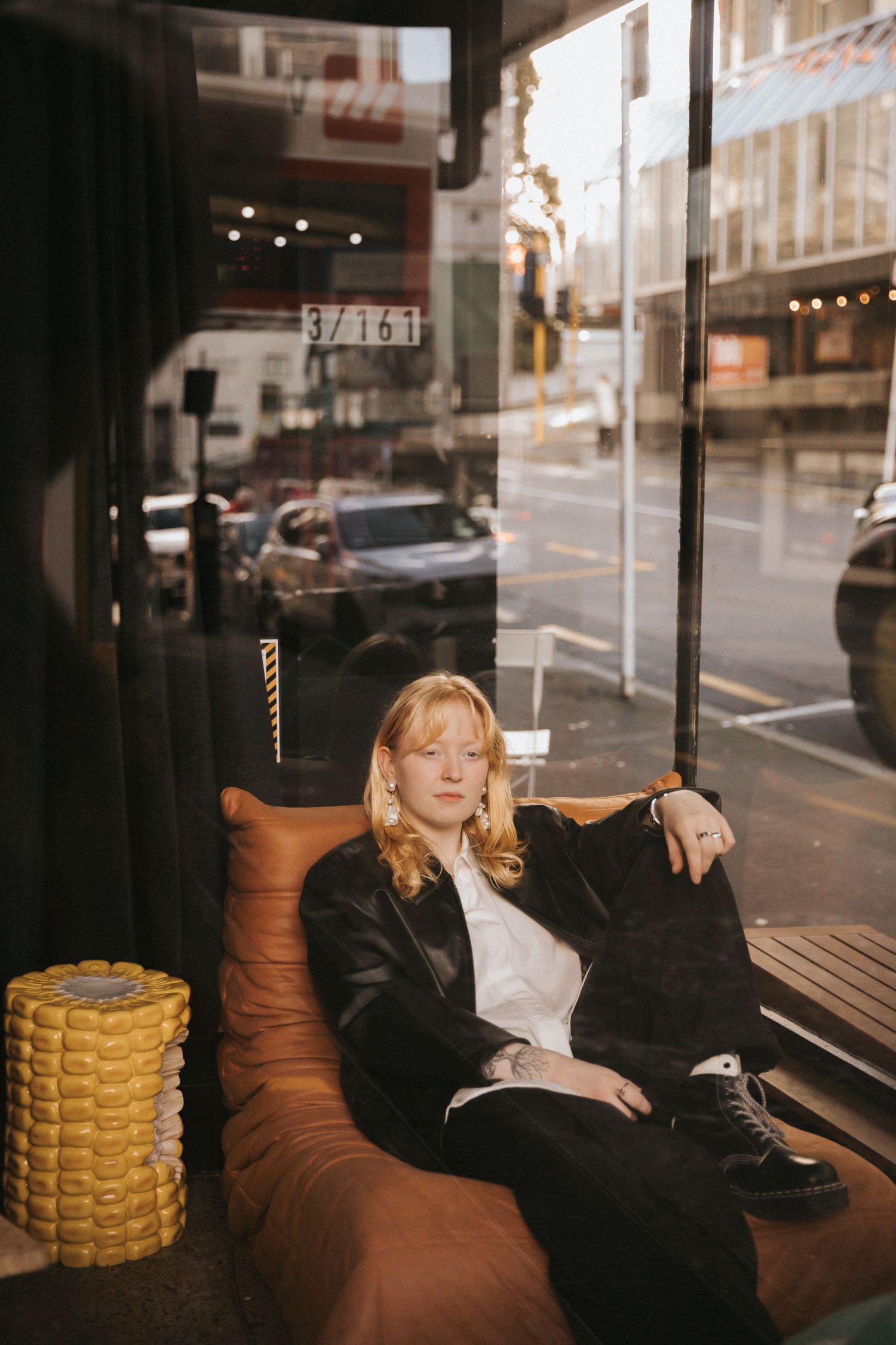 Cozy cafe interior with brown lounge seating by window overlooking urban street with parked cars and city buildings.