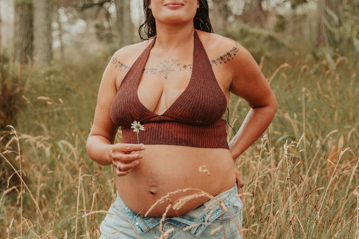 A series of maternity photos showing a pregnant woman in a brown top and jeans posing thoughtfully on a rainy day in the forest.