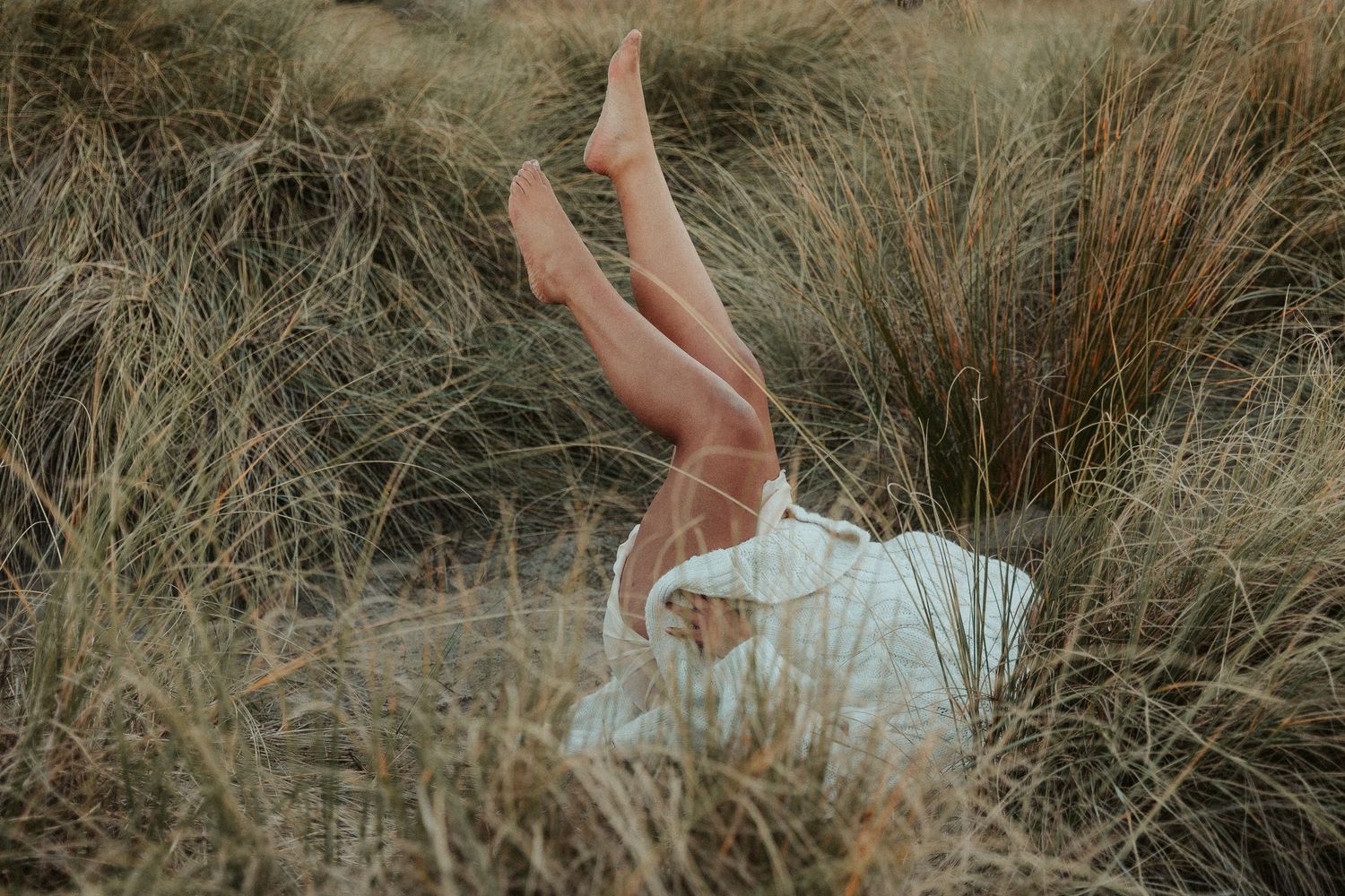 Person in white dress sits gracefully among tall dried grass.