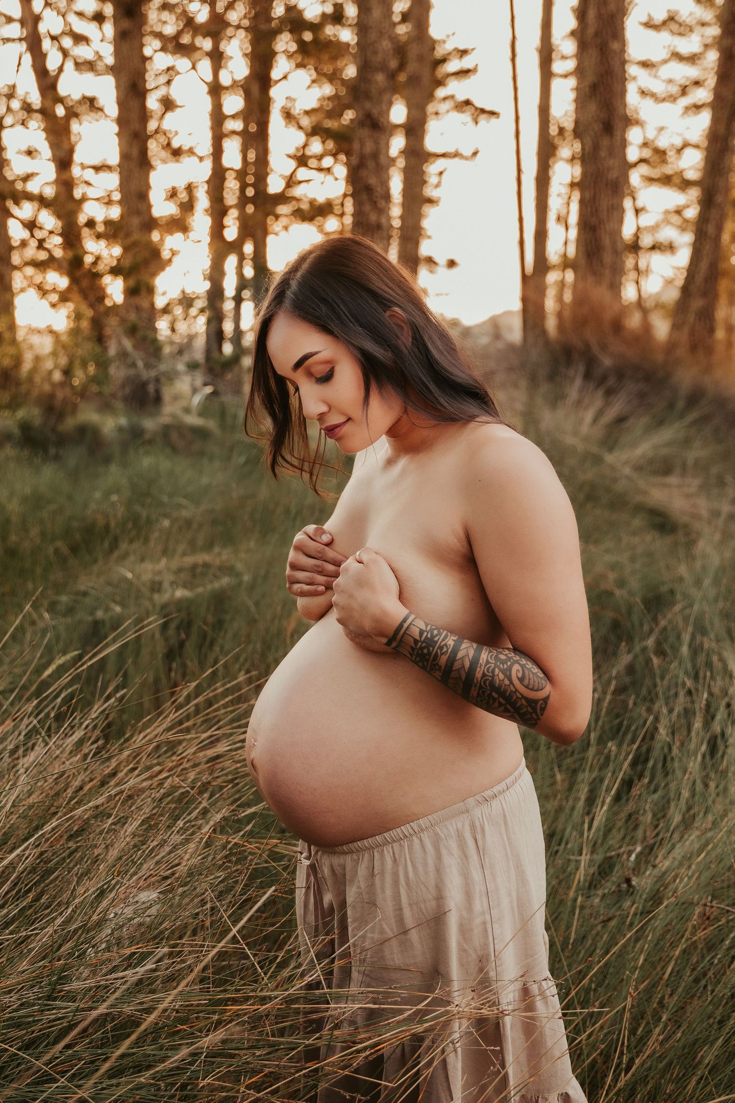 Sunset maternity photography in tall grass with pine trees silhouetted in background.