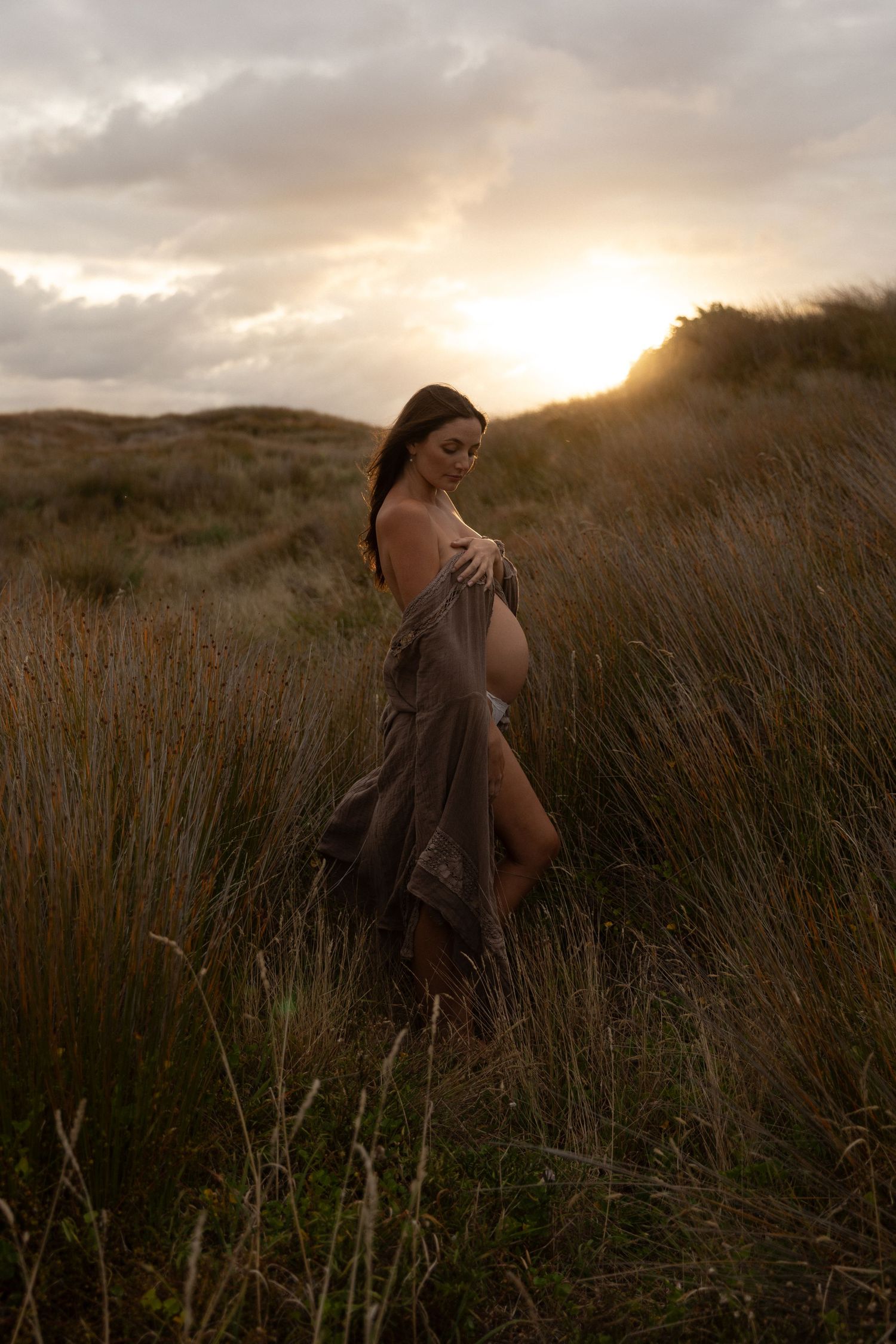 Sunset maternity photography with dramatic backlighting in a wild grass field.