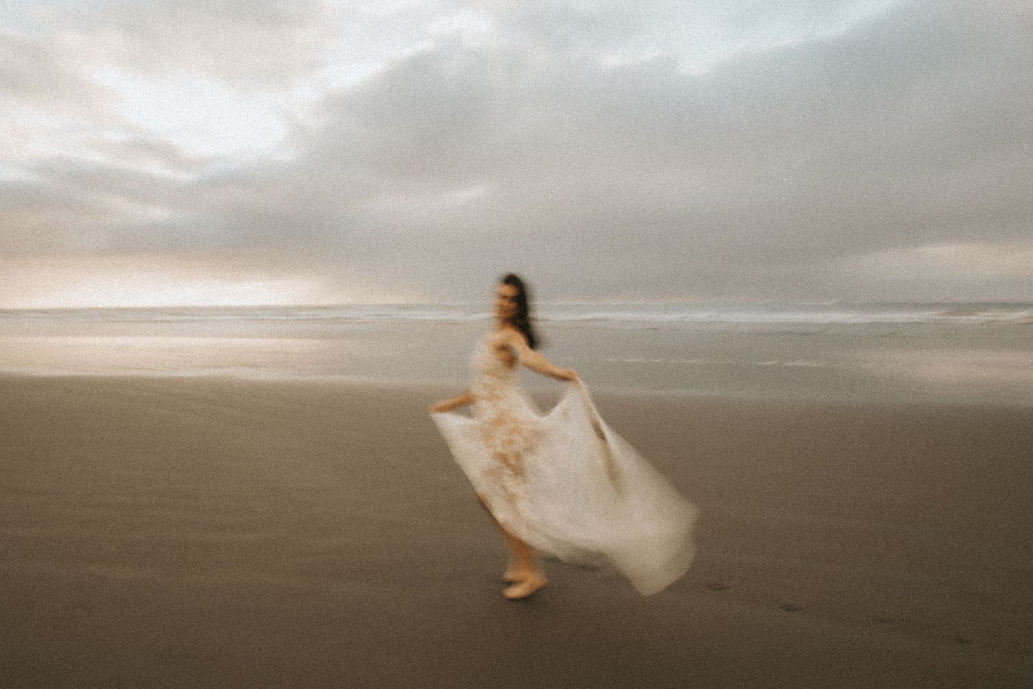 Wide landscape shot of bride dancing freely on misty coastal shoreline.