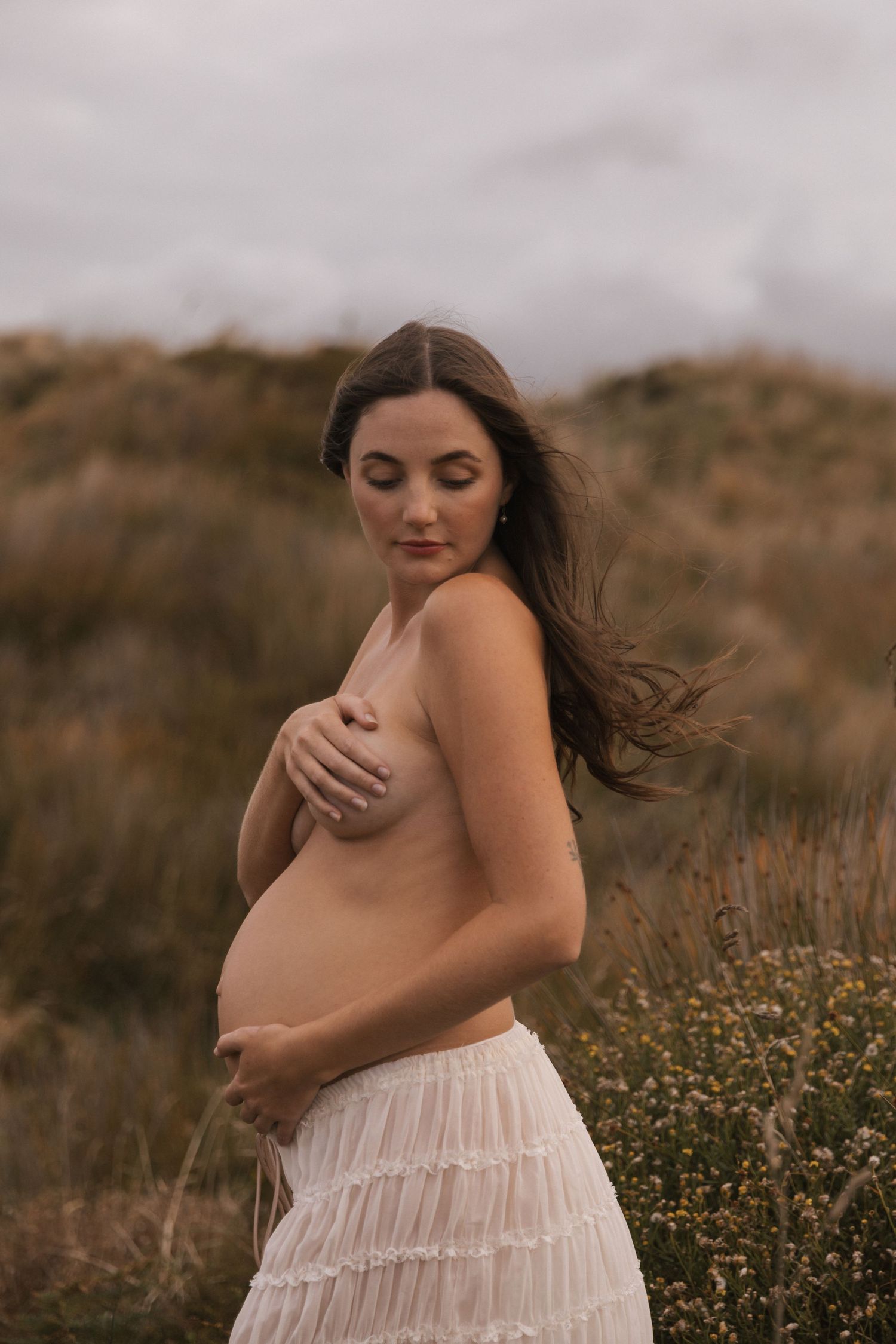 Intimate maternity portrait session in a natural meadow setting with flowing white dress.