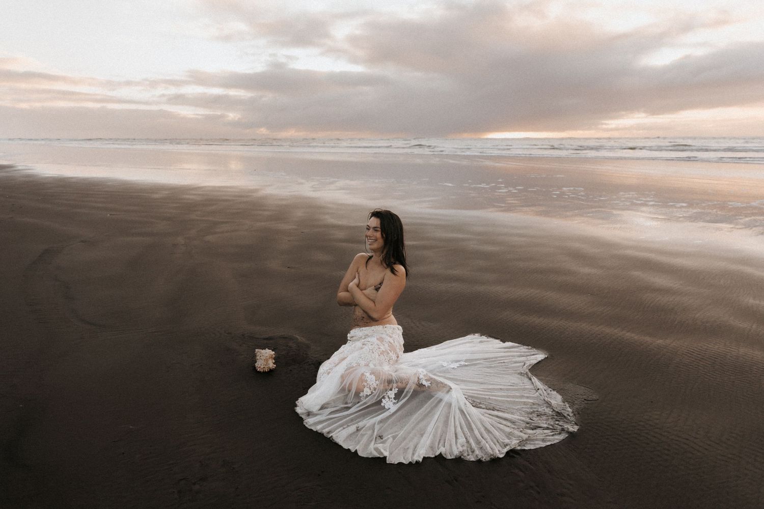 Dramatic coastal landscape with cloudy skies and white dress contrasting against dark beach sand.