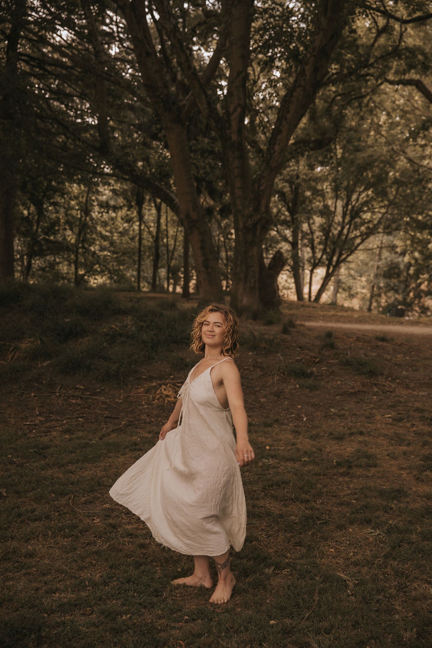 A graceful dance-like pose captured in a wooded setting with warm lighting.
