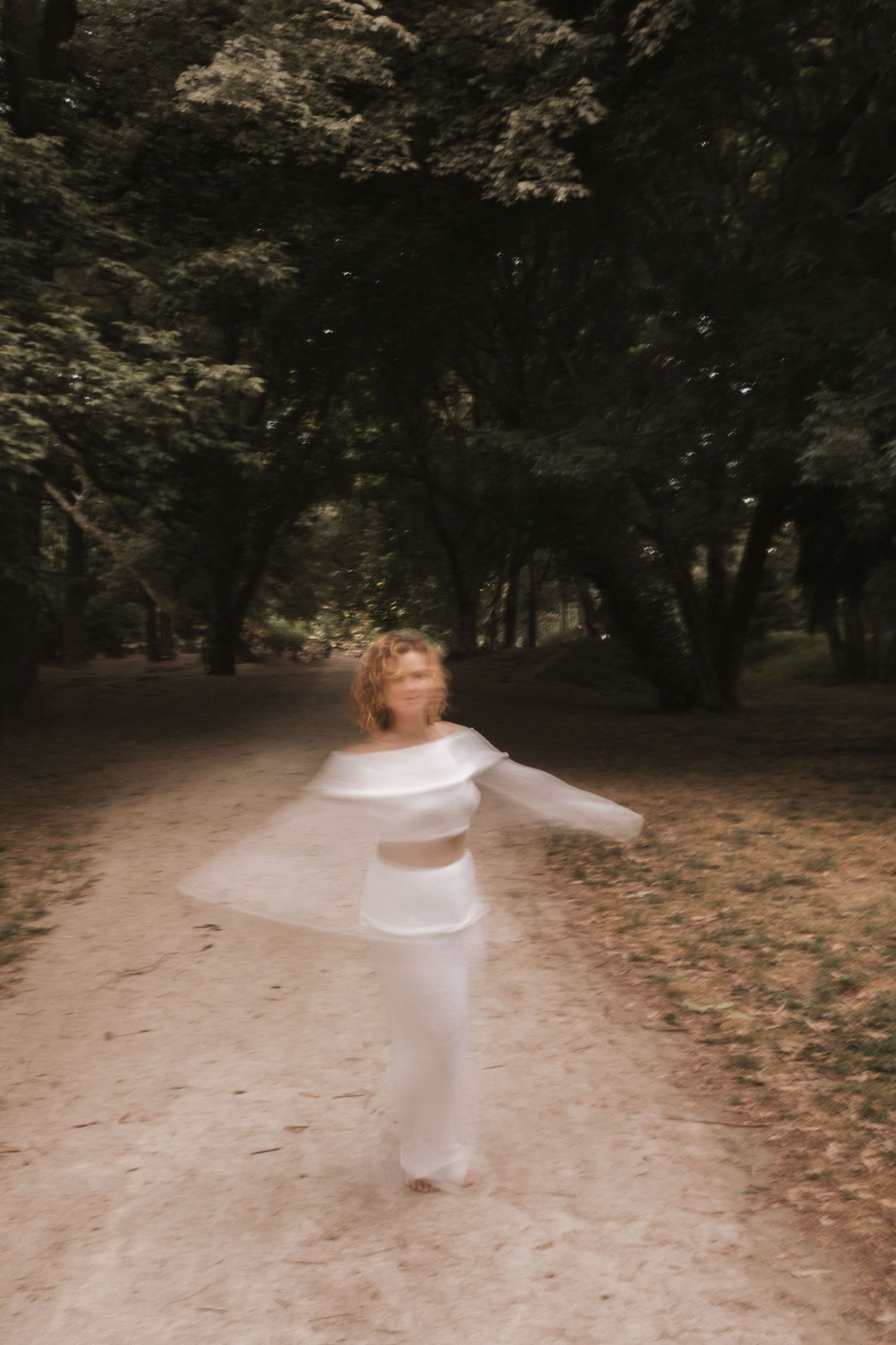Blurred motion shot of person in white outfit spinning in wooded area.