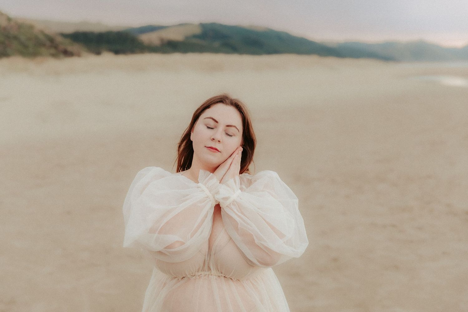 Romantic coastal photoshoot with flowing dress against sandy dunes and ocean backdrop.