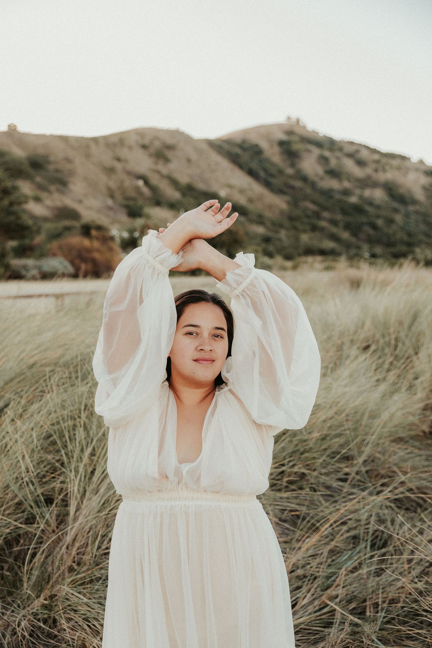 Person in flowing white dress poses gracefully in tall coastal grass.