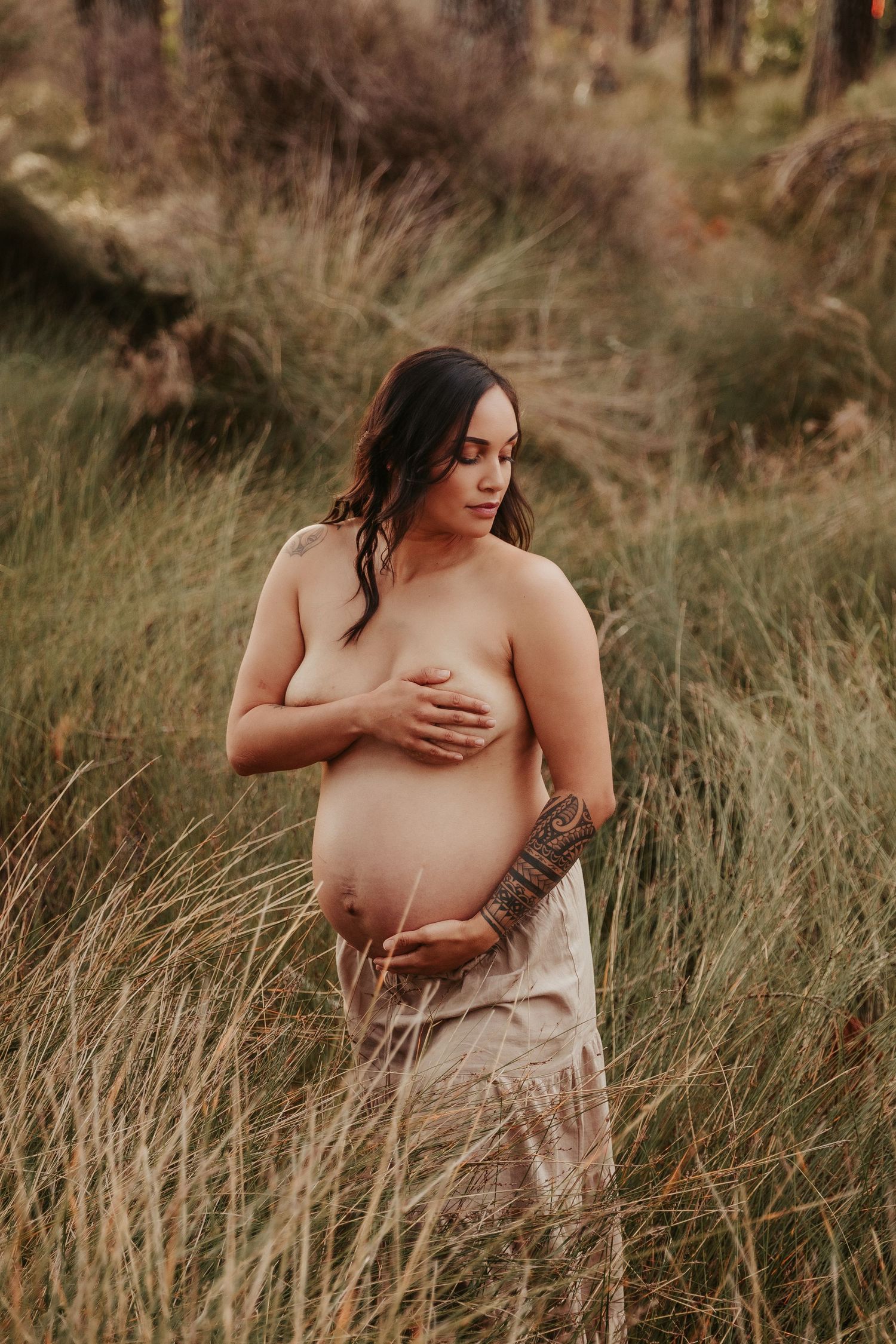 Intimate maternity portrait in rustic outdoor setting with tall grass.