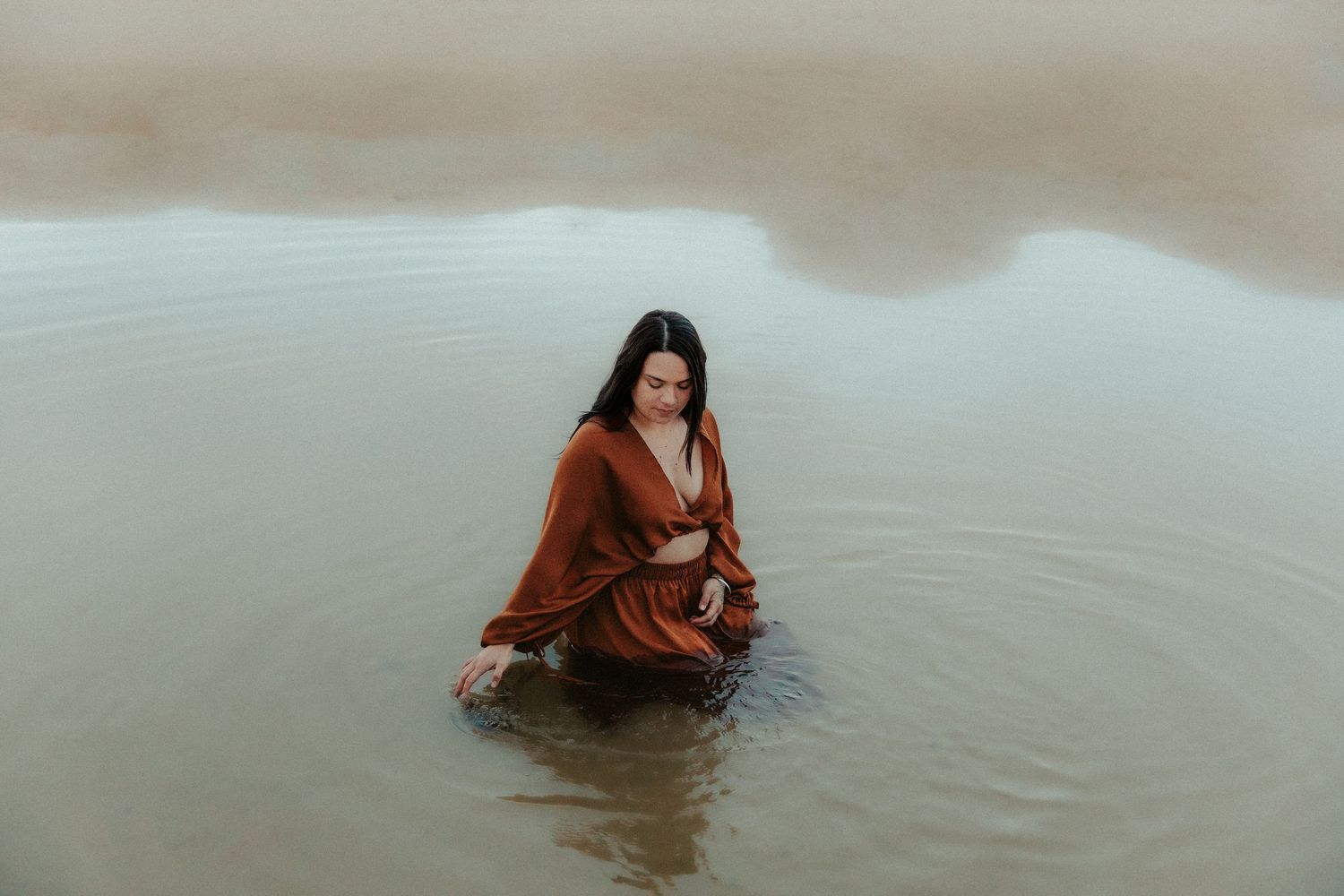 Dramatic water photoshoot with flowing dresses in shallow coastal waters.