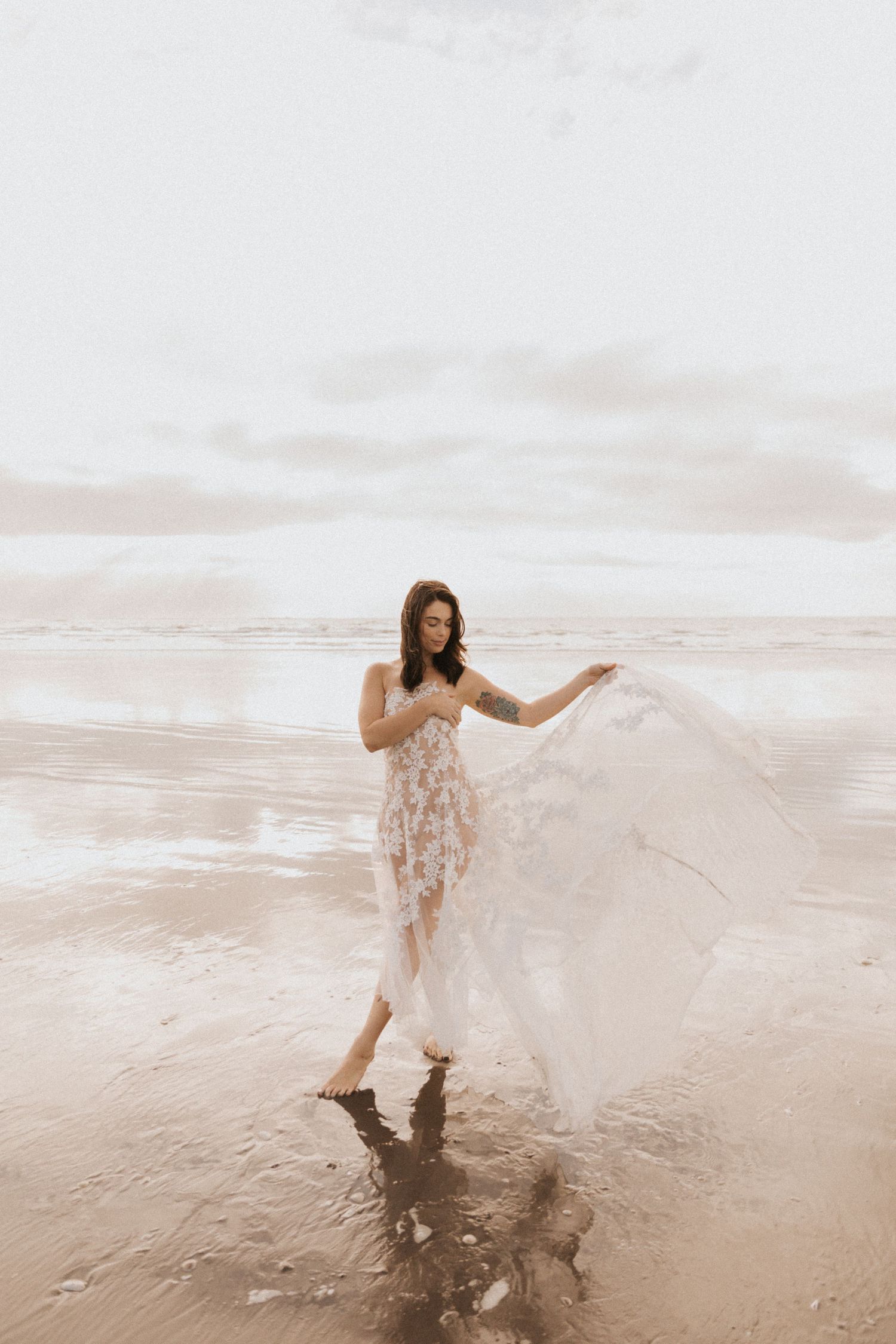 Dreamy coastal photoshoot featuring flowing white lace dress on sandy beach.