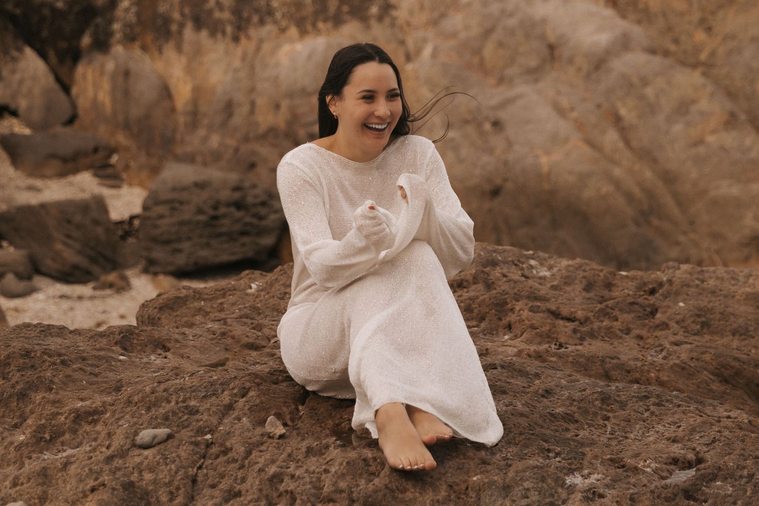 Romantic desert photoshoot featuring flowing white dress against rocky landscape.