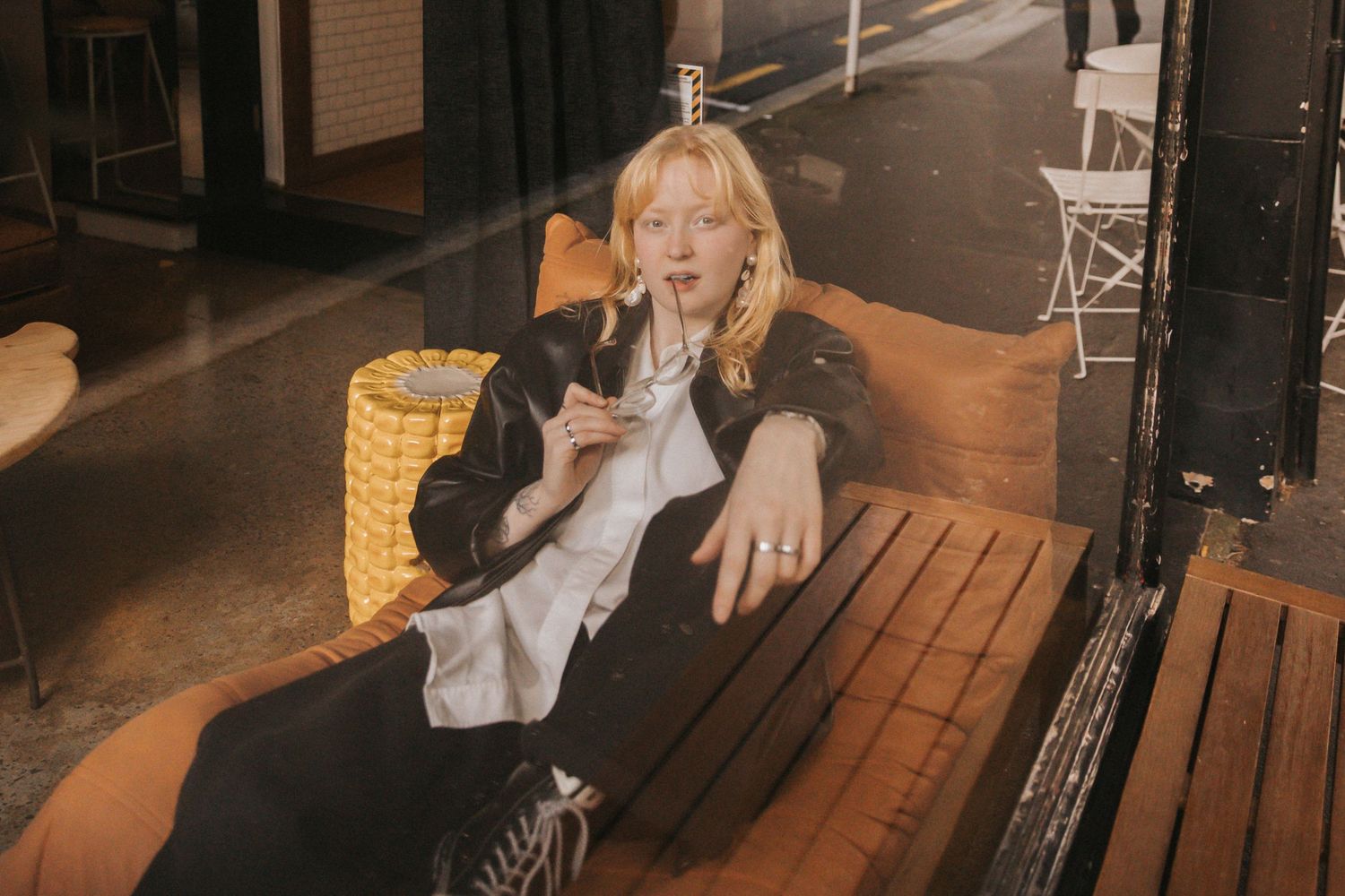 A person sits on a wooden bench in warm lighting while drinking from a paper cup.