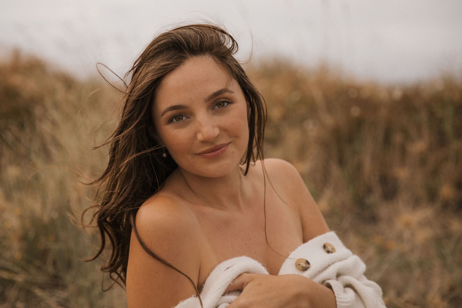 Ethereal maternity portrait with windswept hair against natural coastal backdrop.