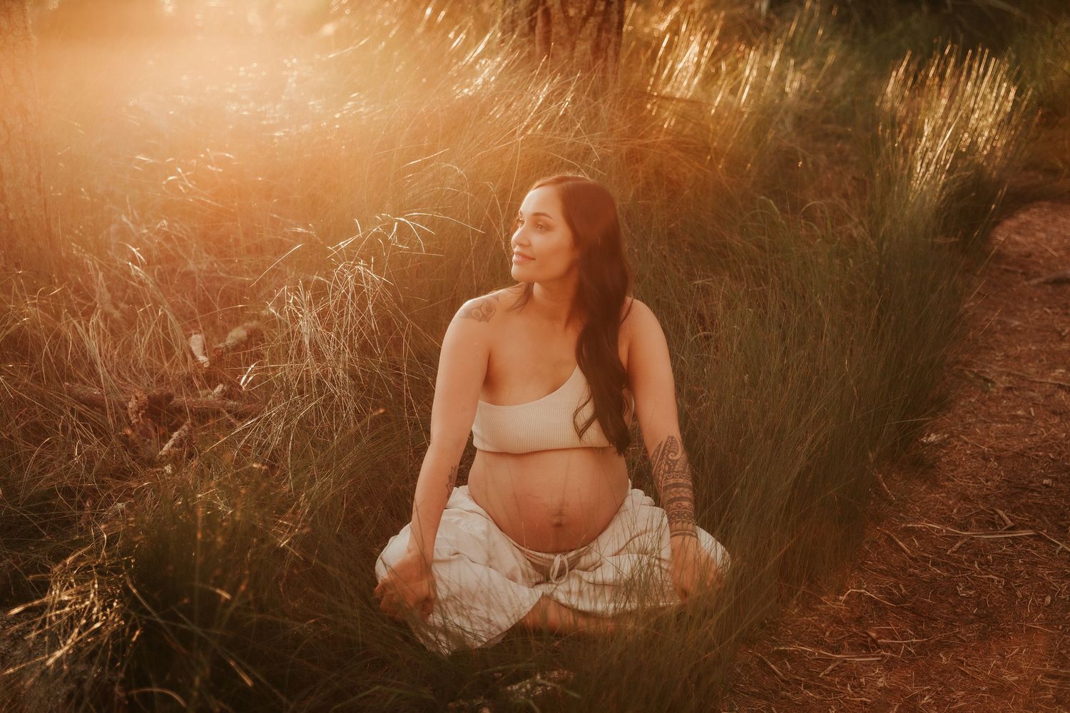 Woman in white dress sitting in golden sunlight during sunset photoshoot.