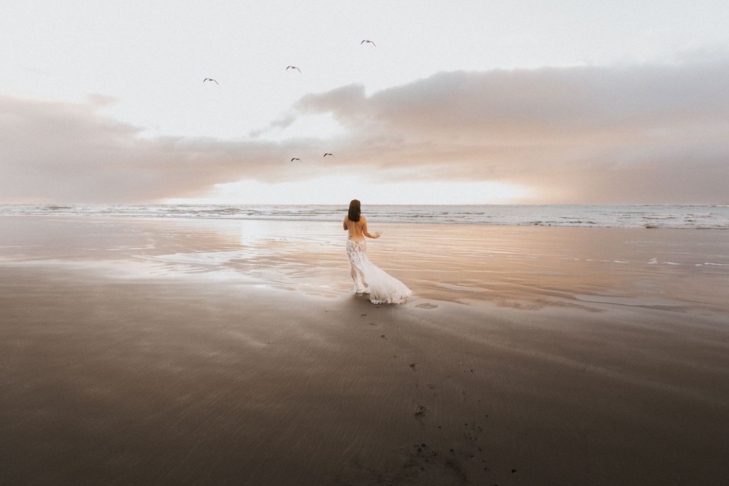 Wide angle beach landscape with distant figure in white against moody sky.
