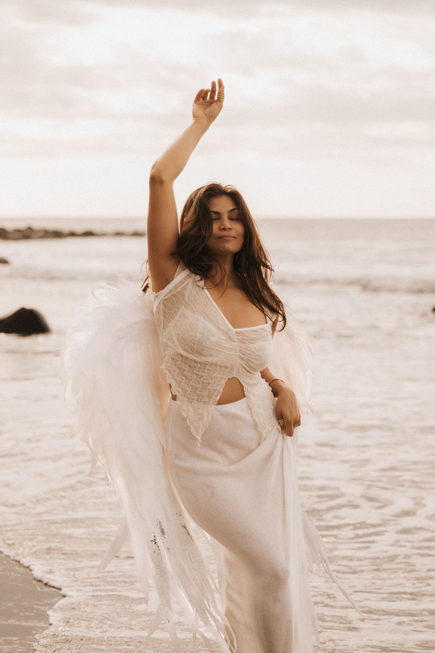 A person in a flowing white dress dances gracefully on a beach at sunset, creating an ethereal and romantic scene.