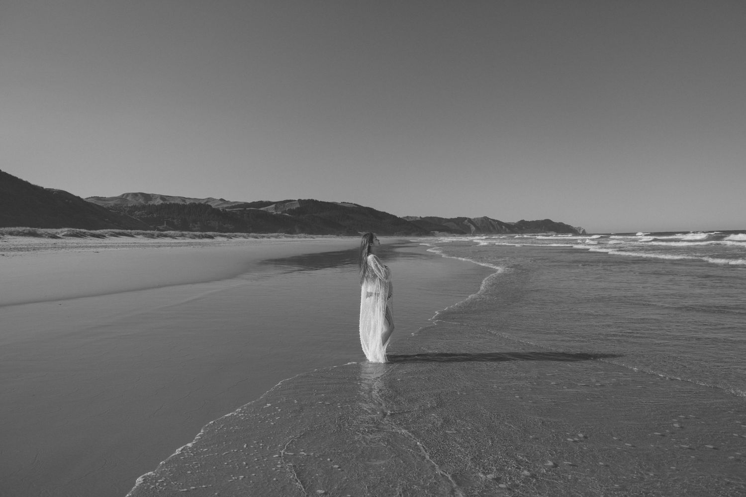 Black and white coastal landscape with distant figure walking on empty beach.