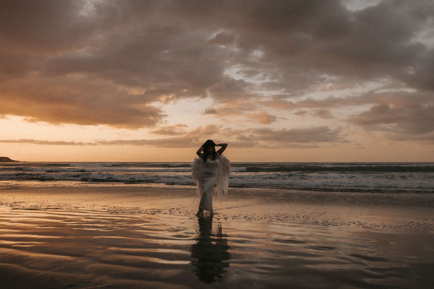 Silhouetted figures on a beach during a dramatic orange sunset with waves crashing on the shore.