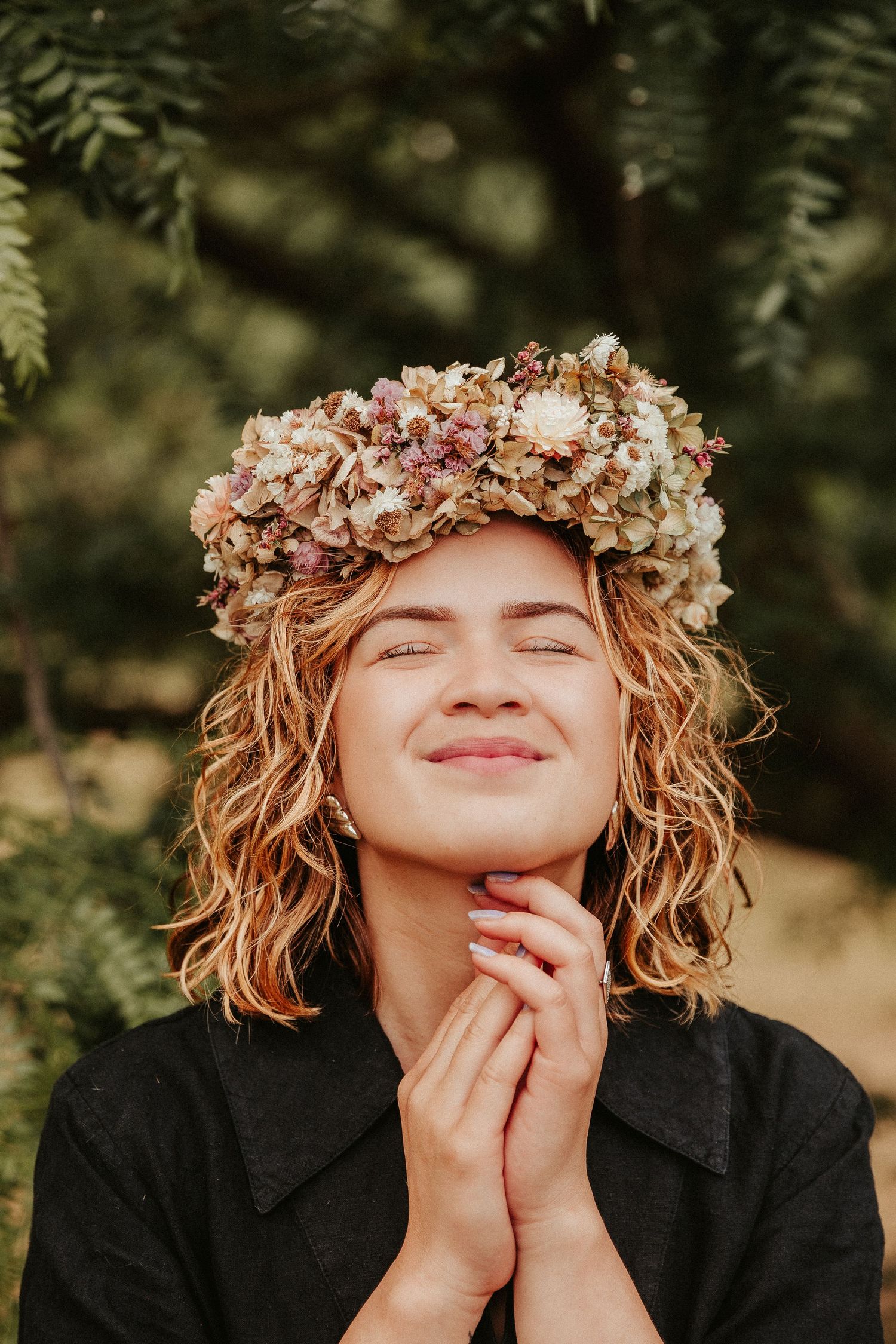 Person wearing dried flower crown smiles contentedly against natural backdrop.