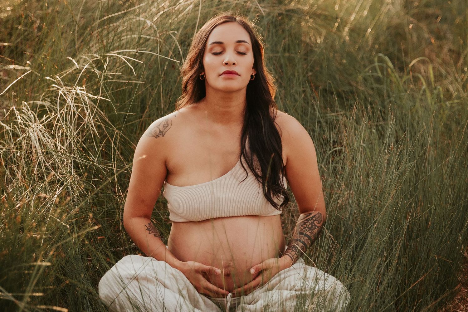 Natural outdoor maternity session among tall grass at golden hour.