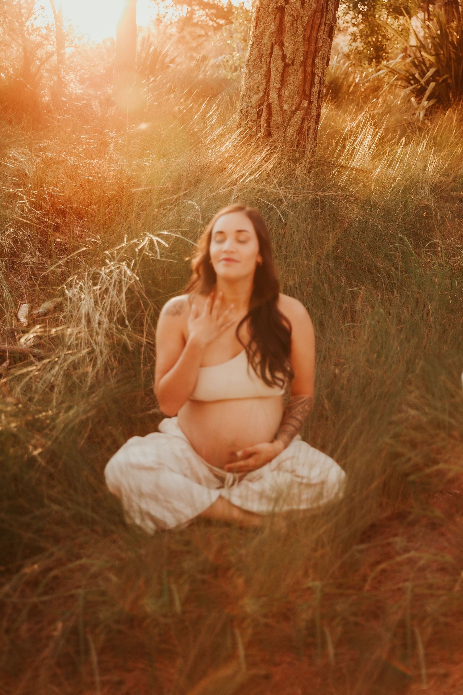 Ethereal maternity photoshoot in tall grass during golden hour sunset with warm glowing light.