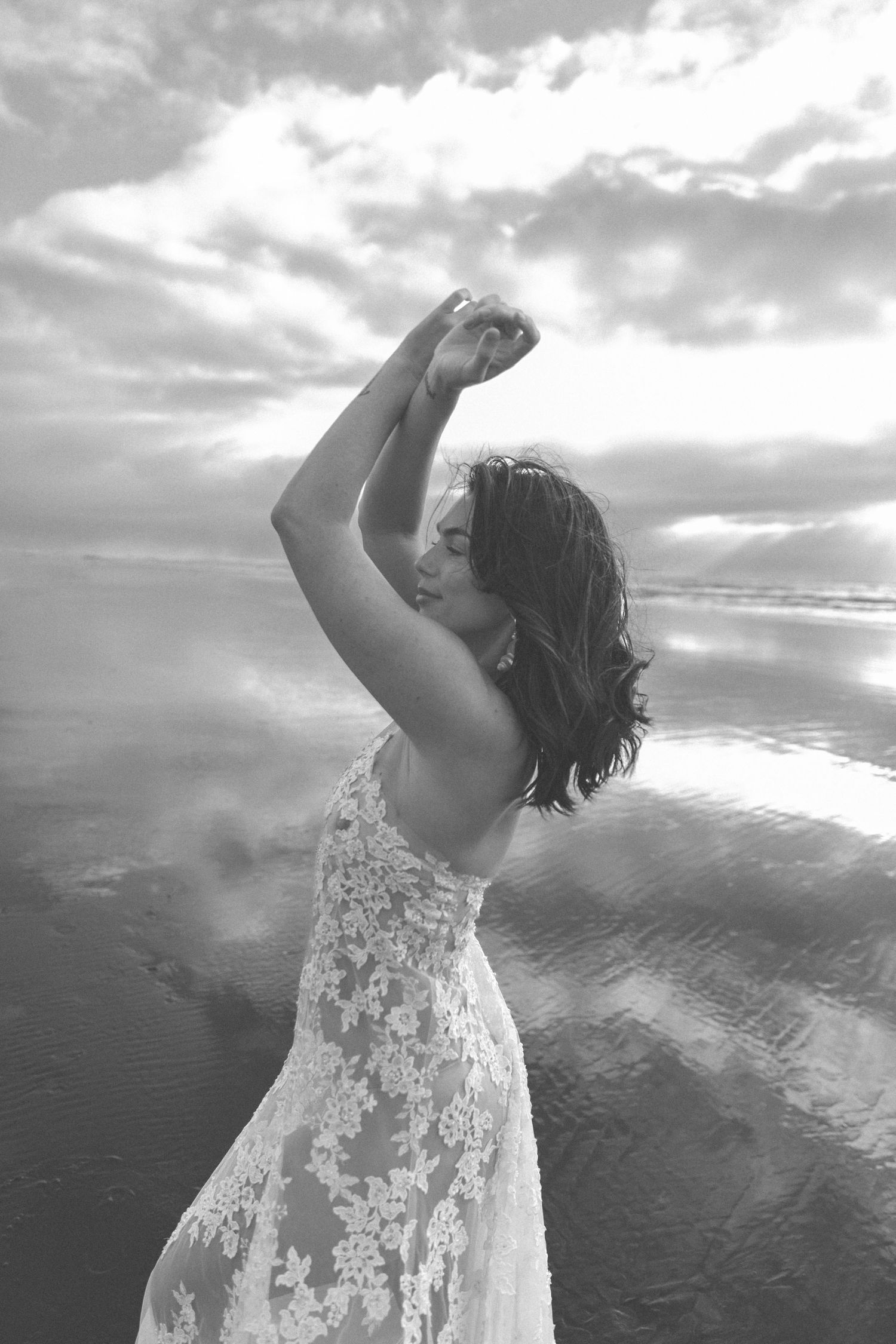 Ethereal black and white portrait of dancer twirling in lace dress by the ocean.