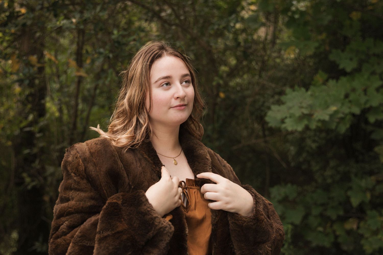 Woman in brown fur coat poses against autumn forest background.