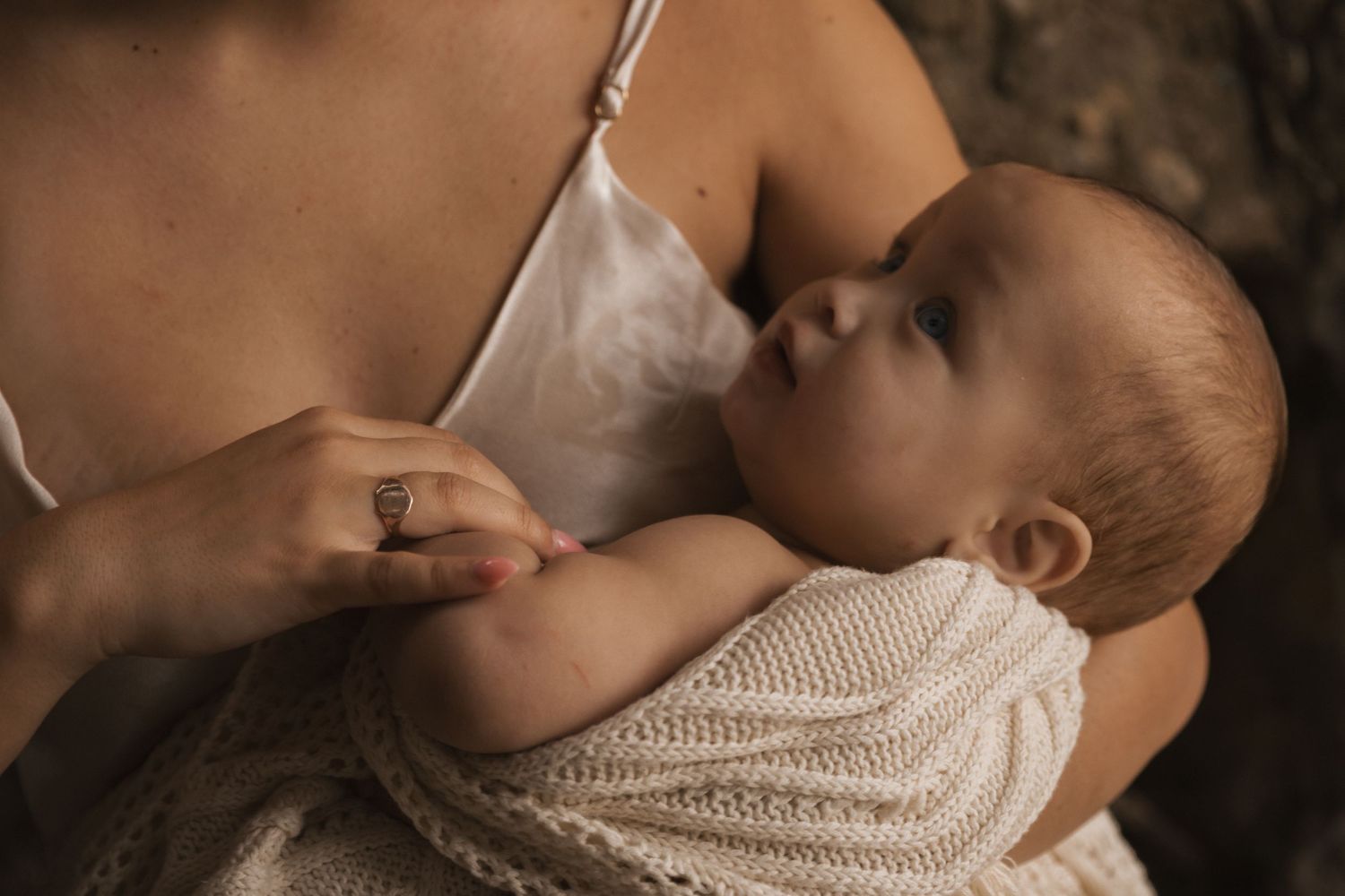 Gentle nursing moment captured in warm earth tones with natural stone backdrop.
