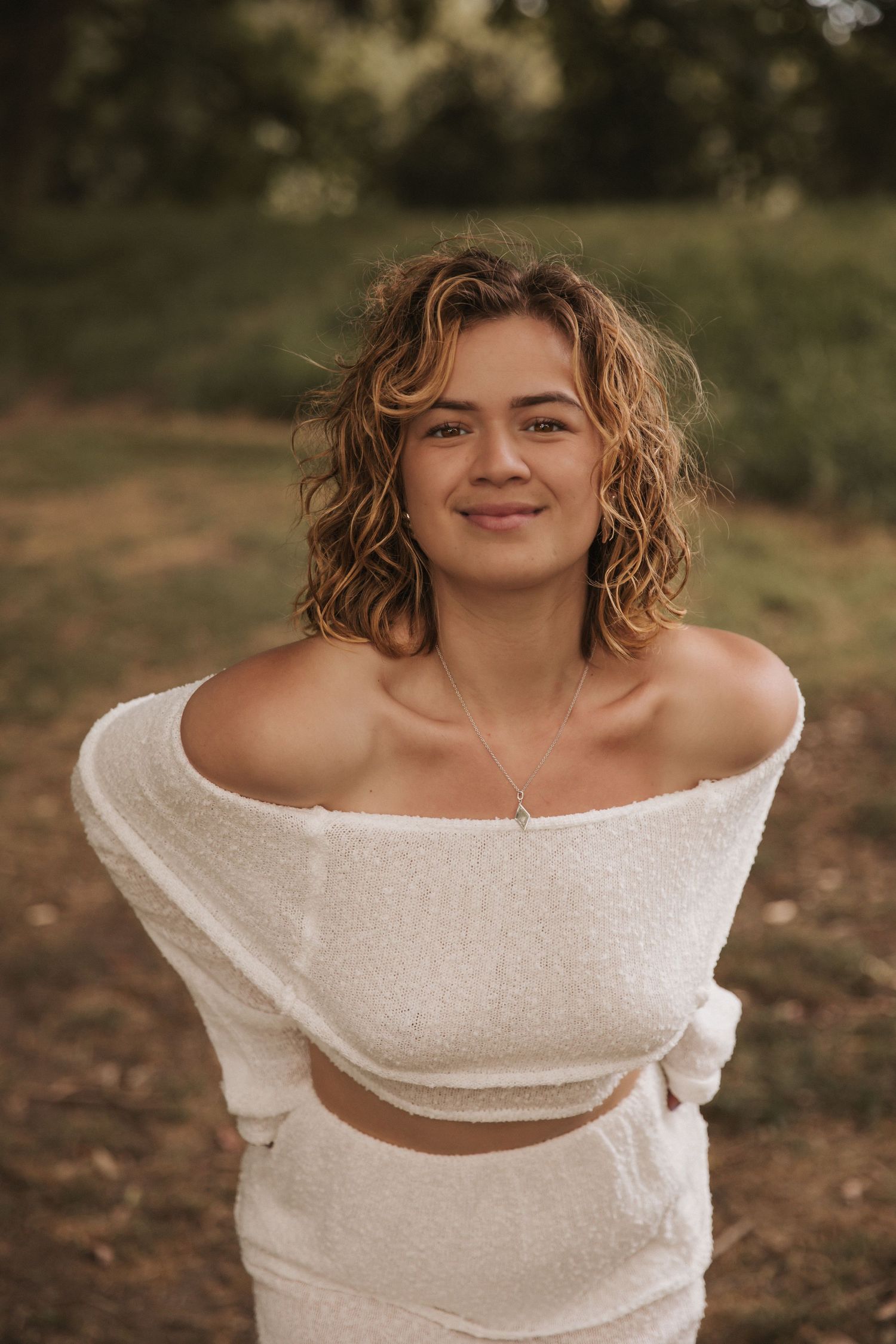 Candid expressions captured in white off-shoulder ensemble against woodland backdrop.