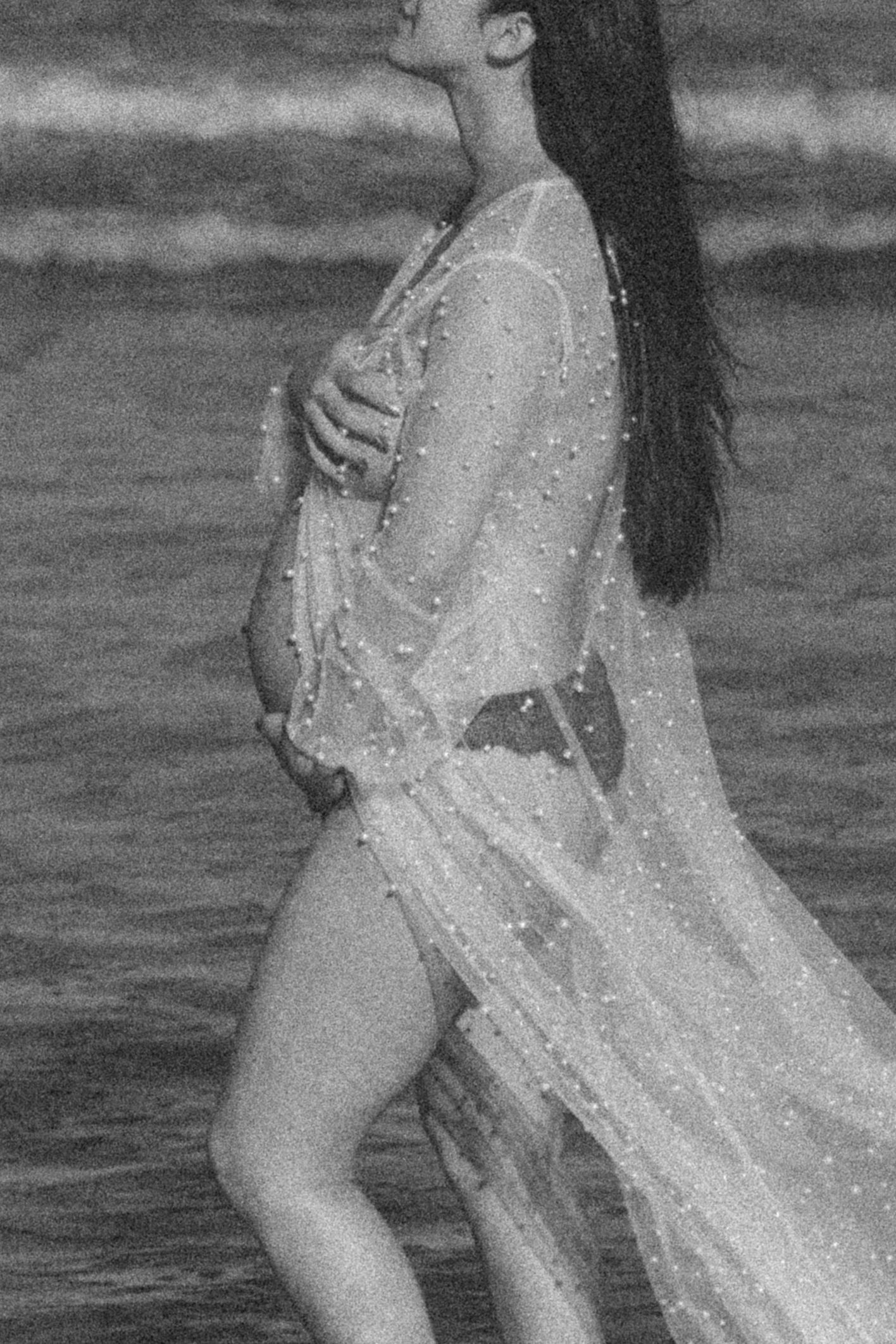 Ethereal black and white maternity portrait in flowing dress by the ocean.