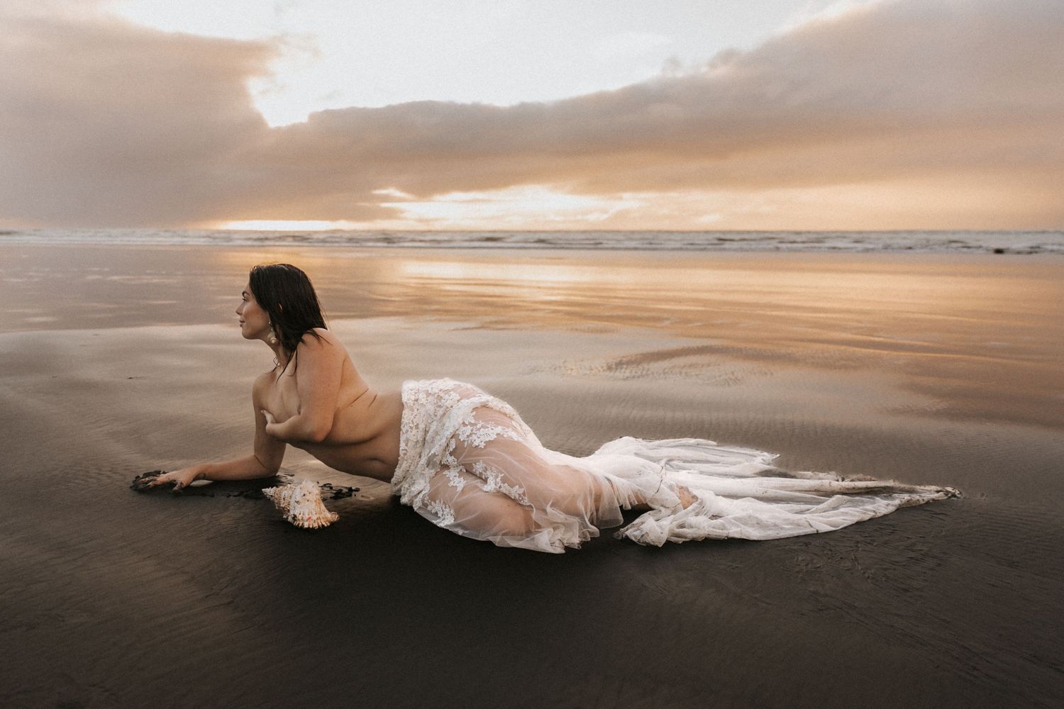 Artistic beach portrait with billowing white dress against golden sunset sky.