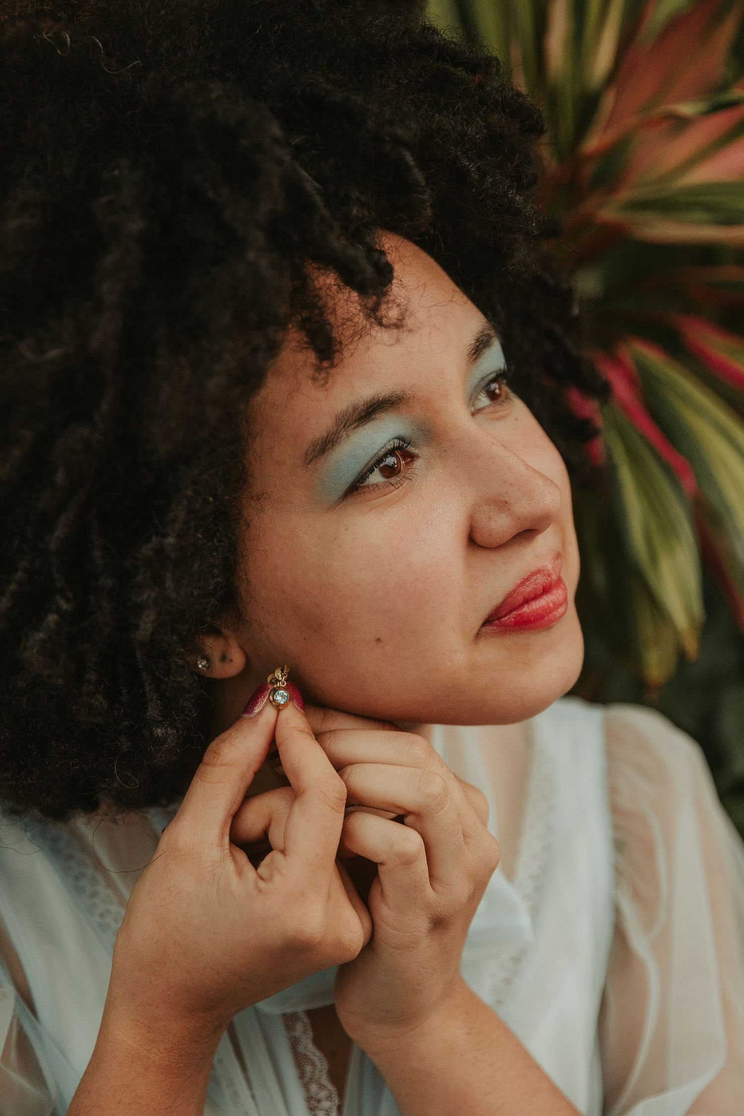 Dreamy portrait with natural curly hair and red lipstick against tropical foliage.