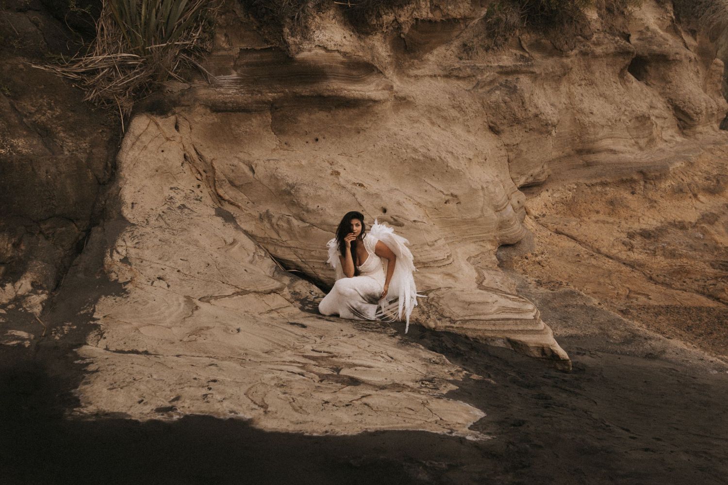 A couple poses together on rocky cliffs near the ocean during a sunset engagement photoshoot session.