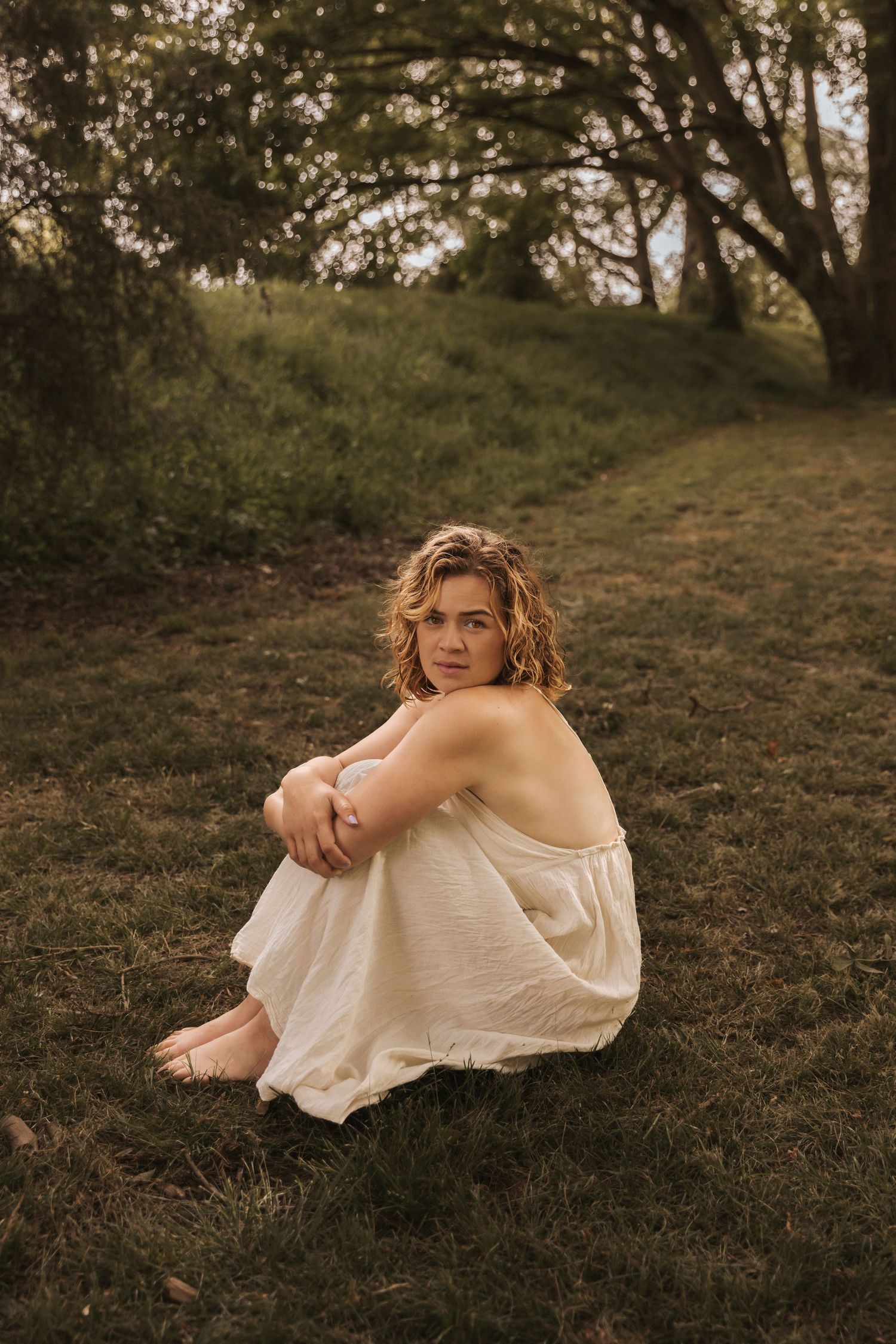 A candid outdoor portrait sitting on a grassy hillside in golden evening light.