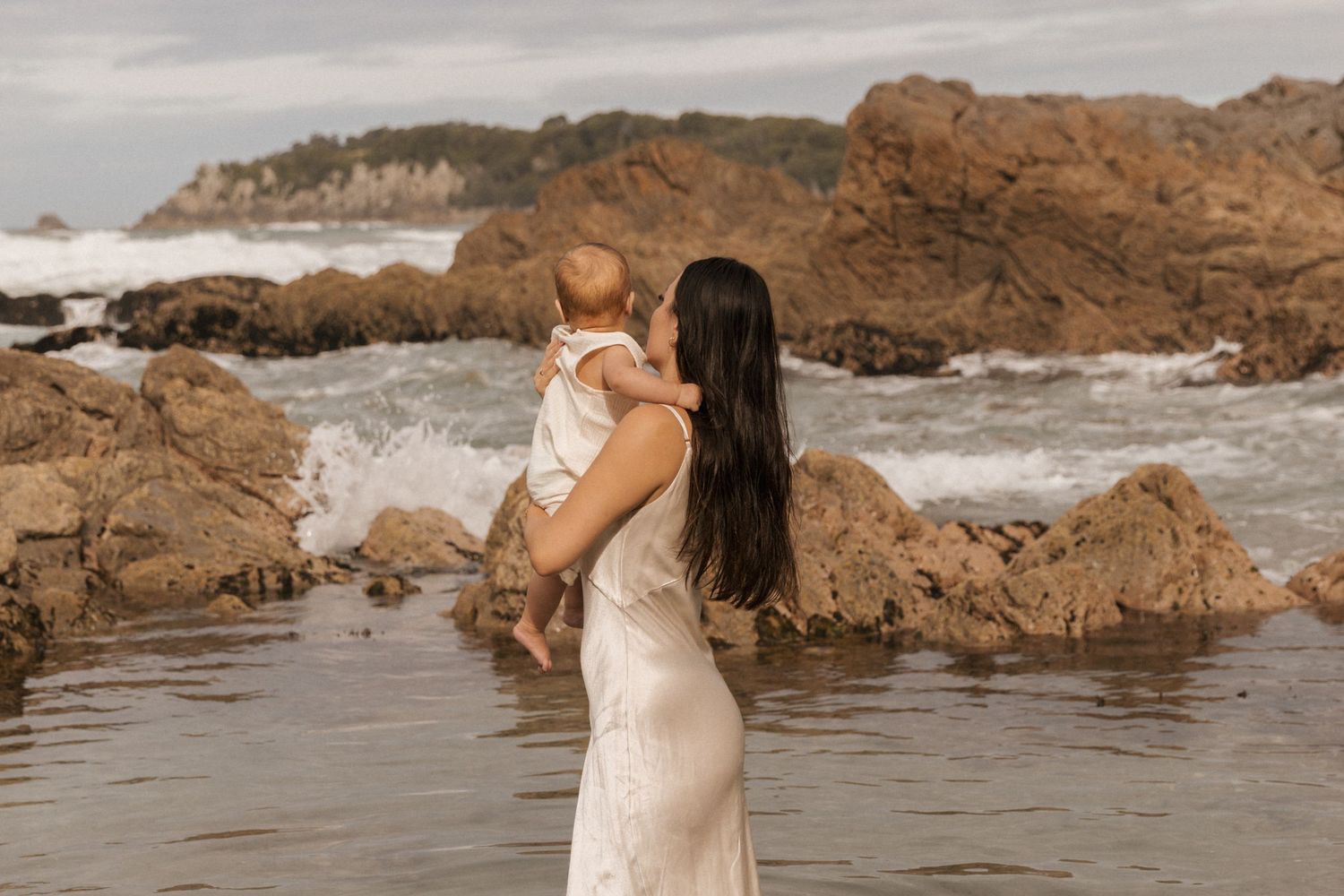 Coastal photoshoot with dramatic rocky cliffs and ocean waves in the background.