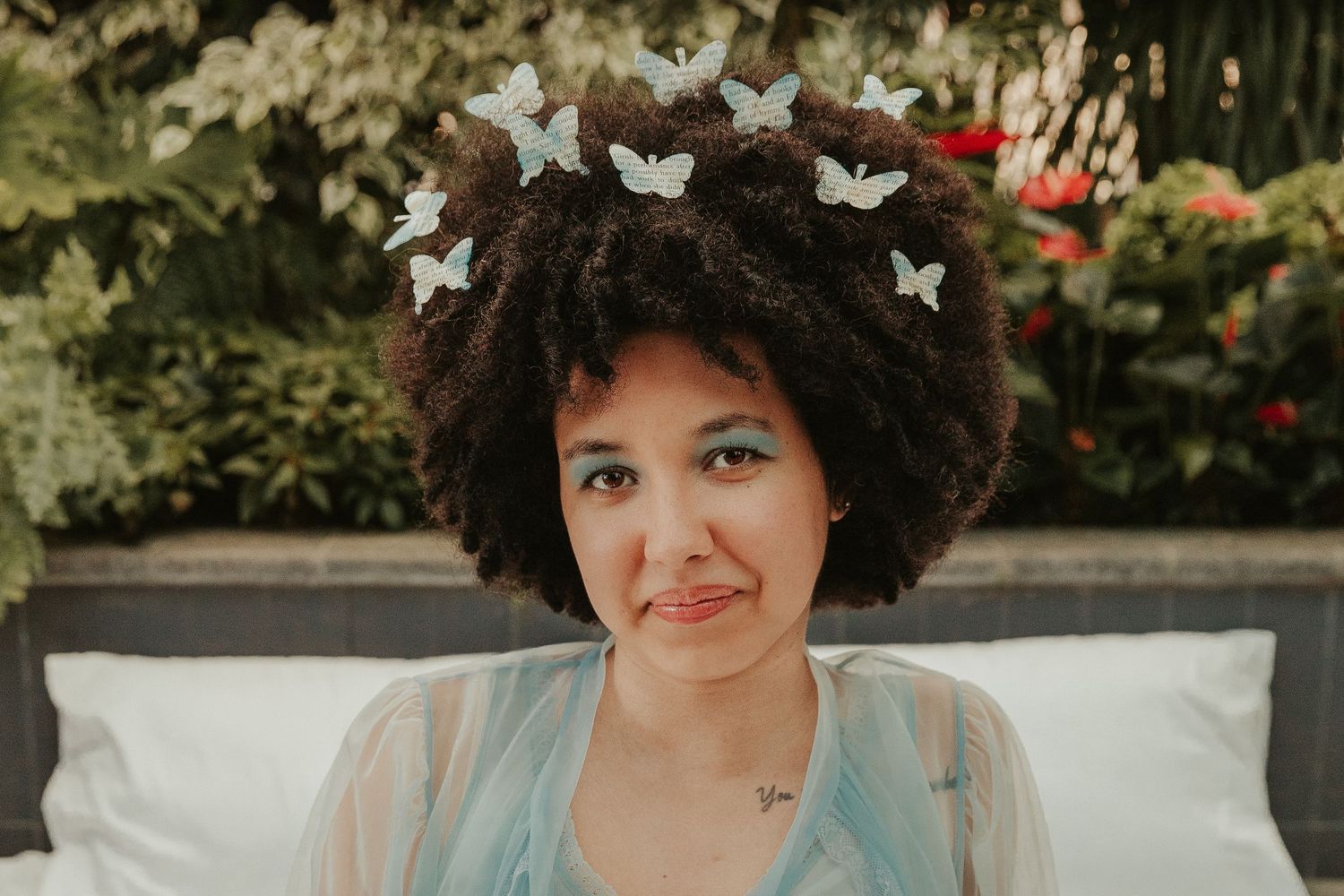 Person with curly hair and butterflies in garden setting.
