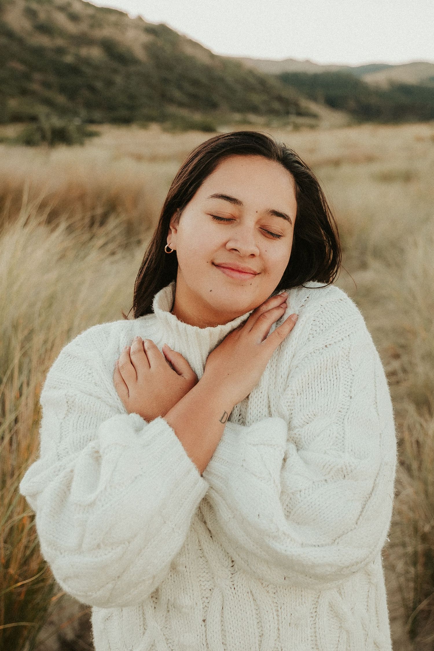 Person in cozy white sweater poses in field of golden grass.