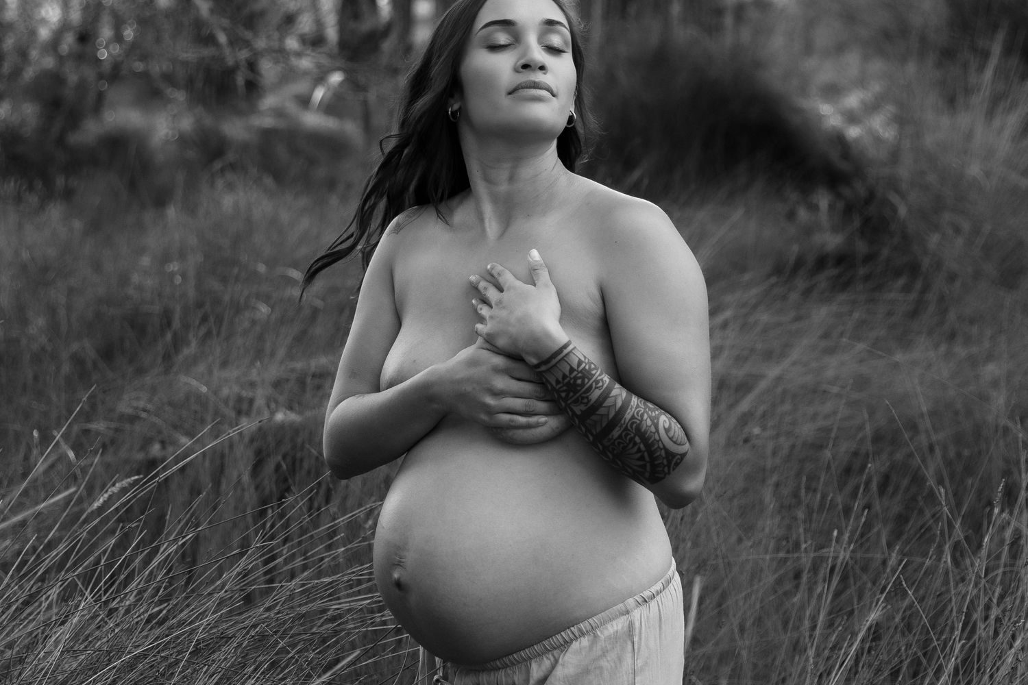 Artistic maternity photoshoot in tall grass at sunset with soft lighting and natural scenery.