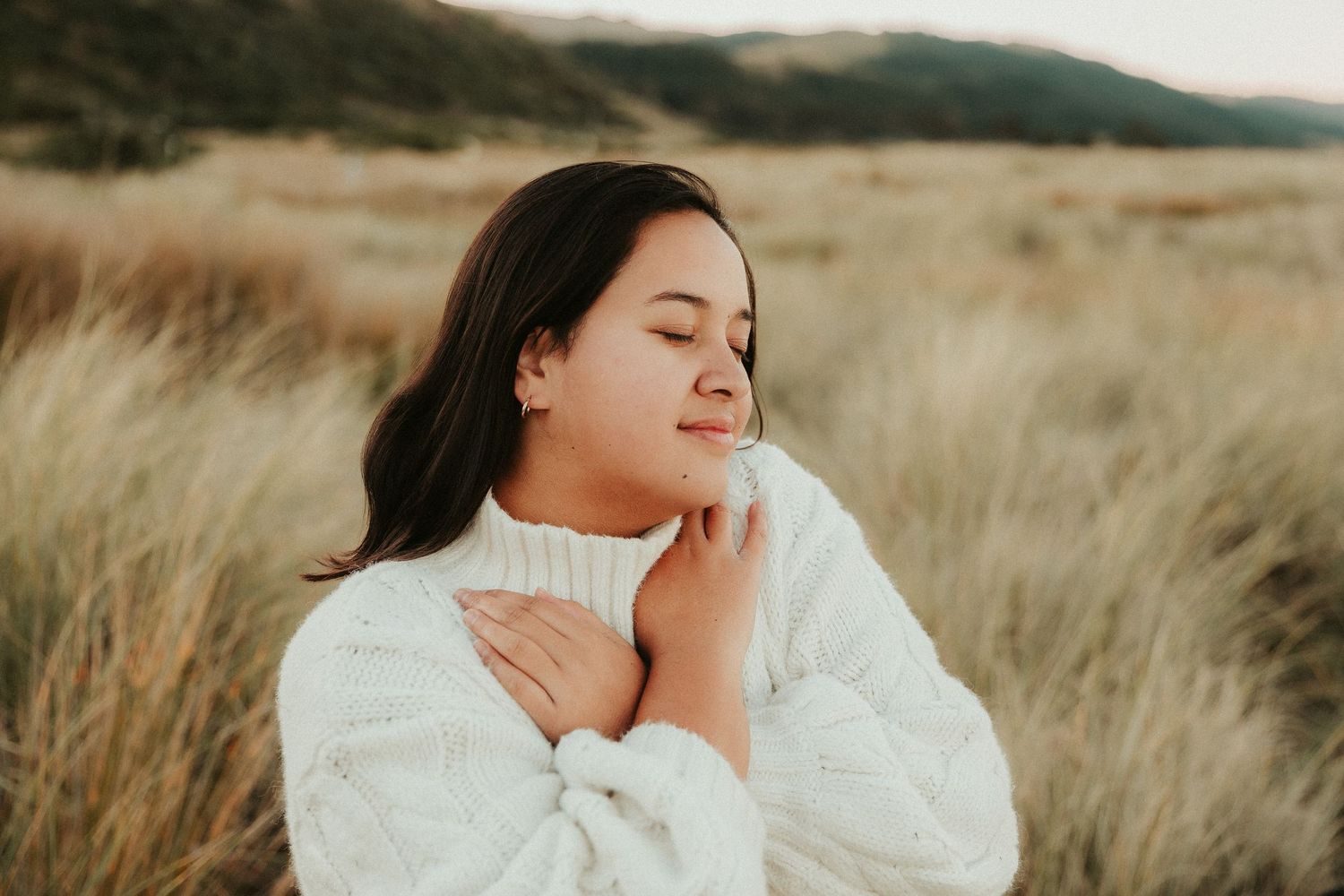 Person in white sweater captured in warm evening light among tall grass.