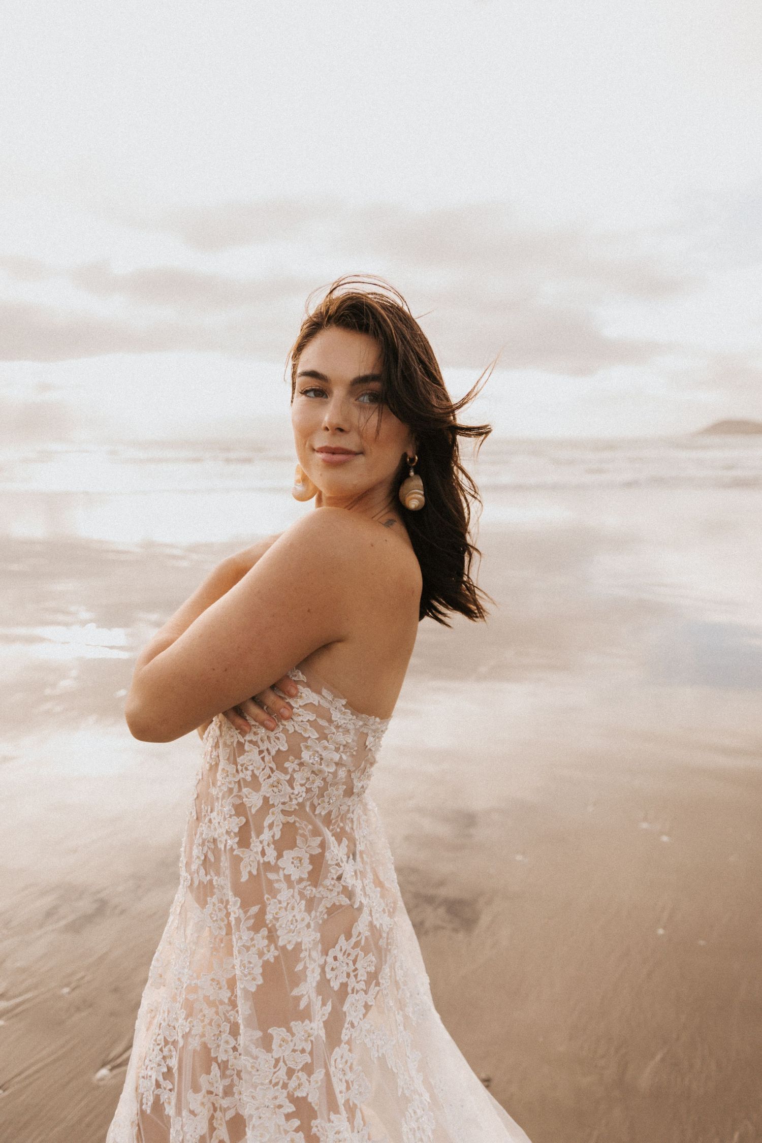 Woman in delicate lace dress poses against sandy beach backdrop.