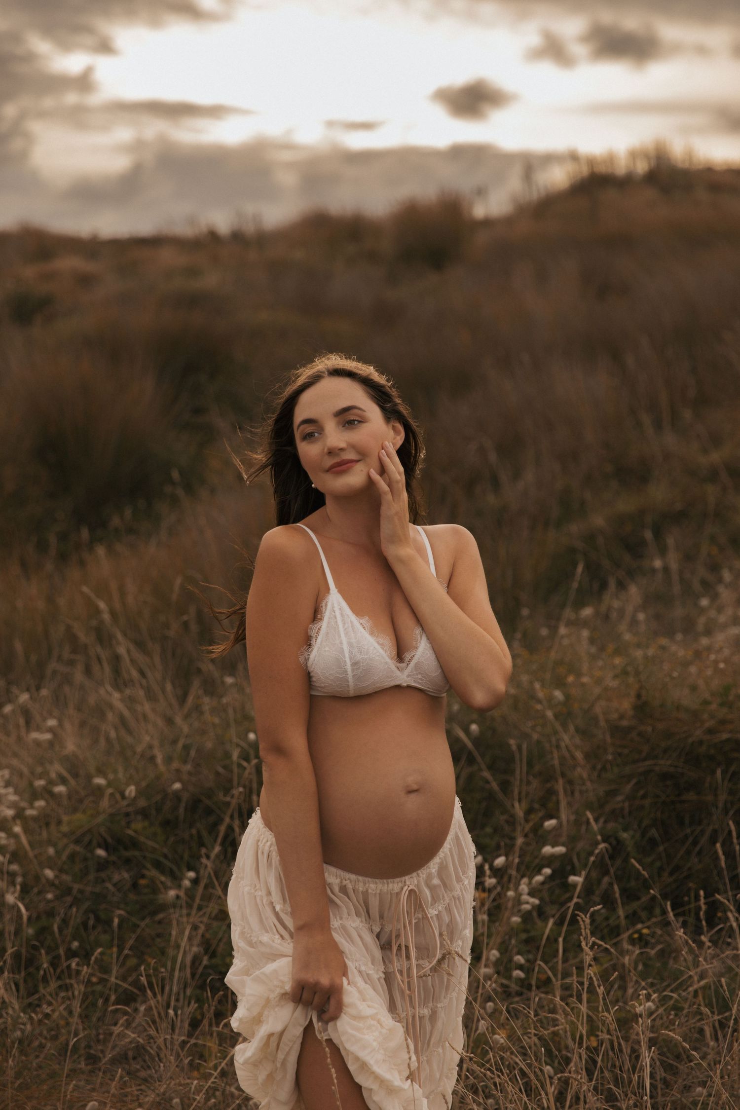 Sunset maternity session showing graceful poses in a field of wild grass.