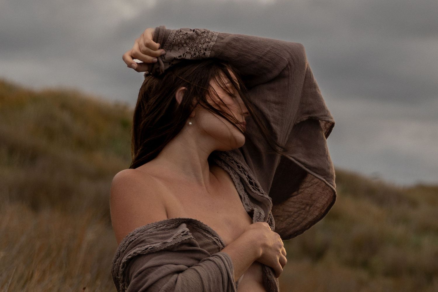 Artistic maternity photoshoot in tall grass field at sunset with moody cloudy sky.