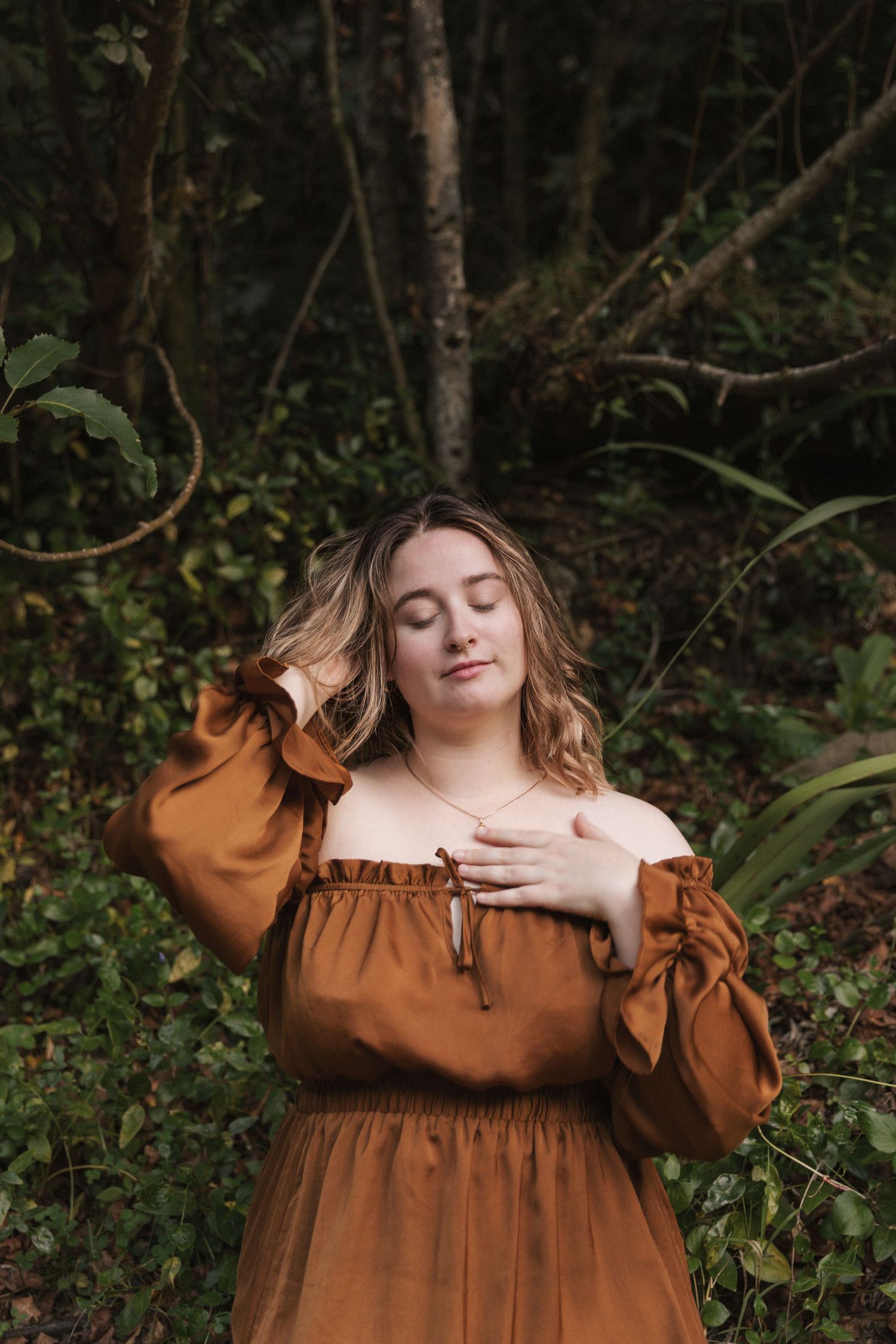 A rustic autumn portrait featuring a brown off-shoulder dress against a dark forest backdrop.